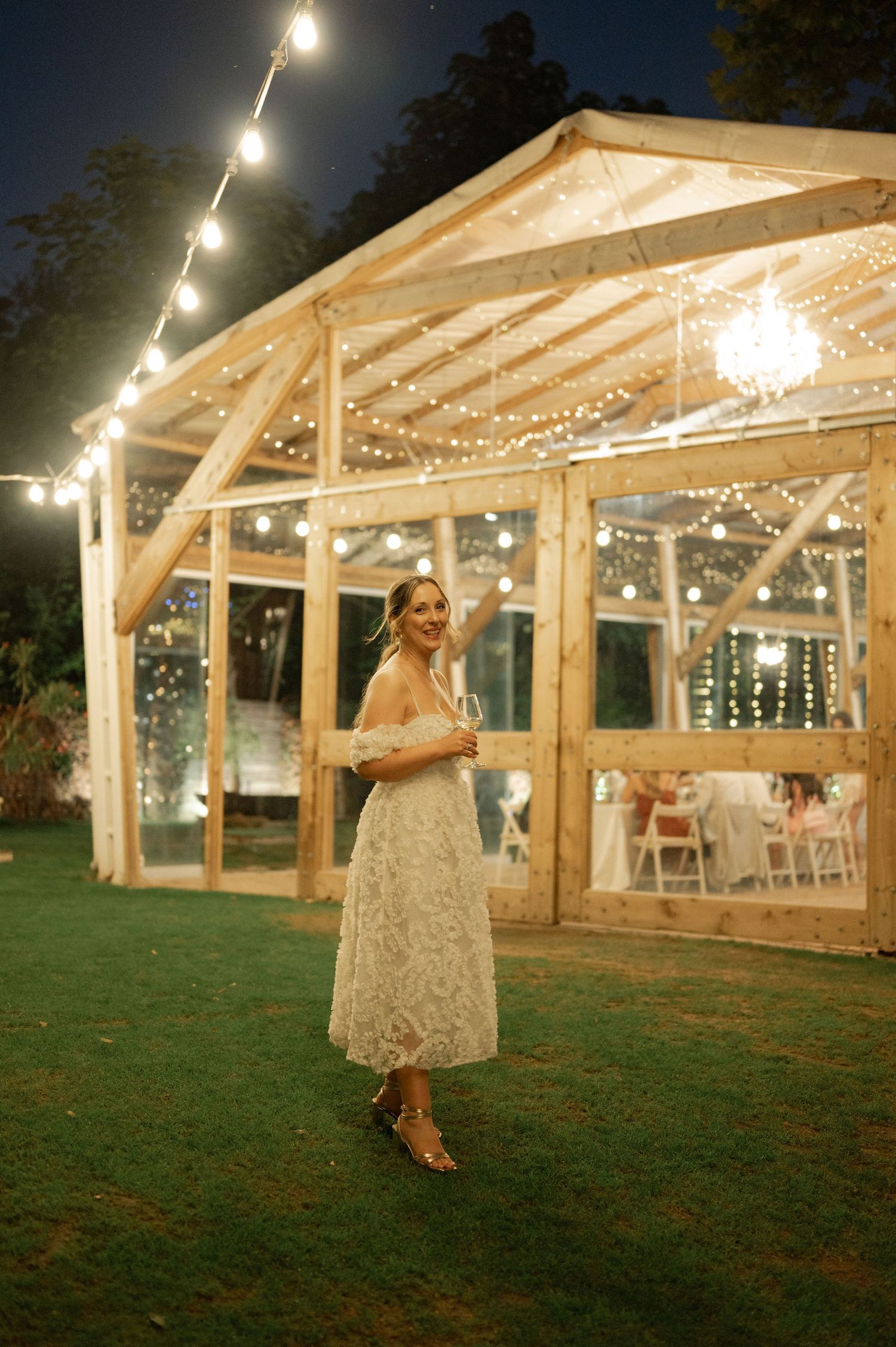 Outdoor wedding venue with wooden pergola and string lights creating a romantic evening atmosphere.