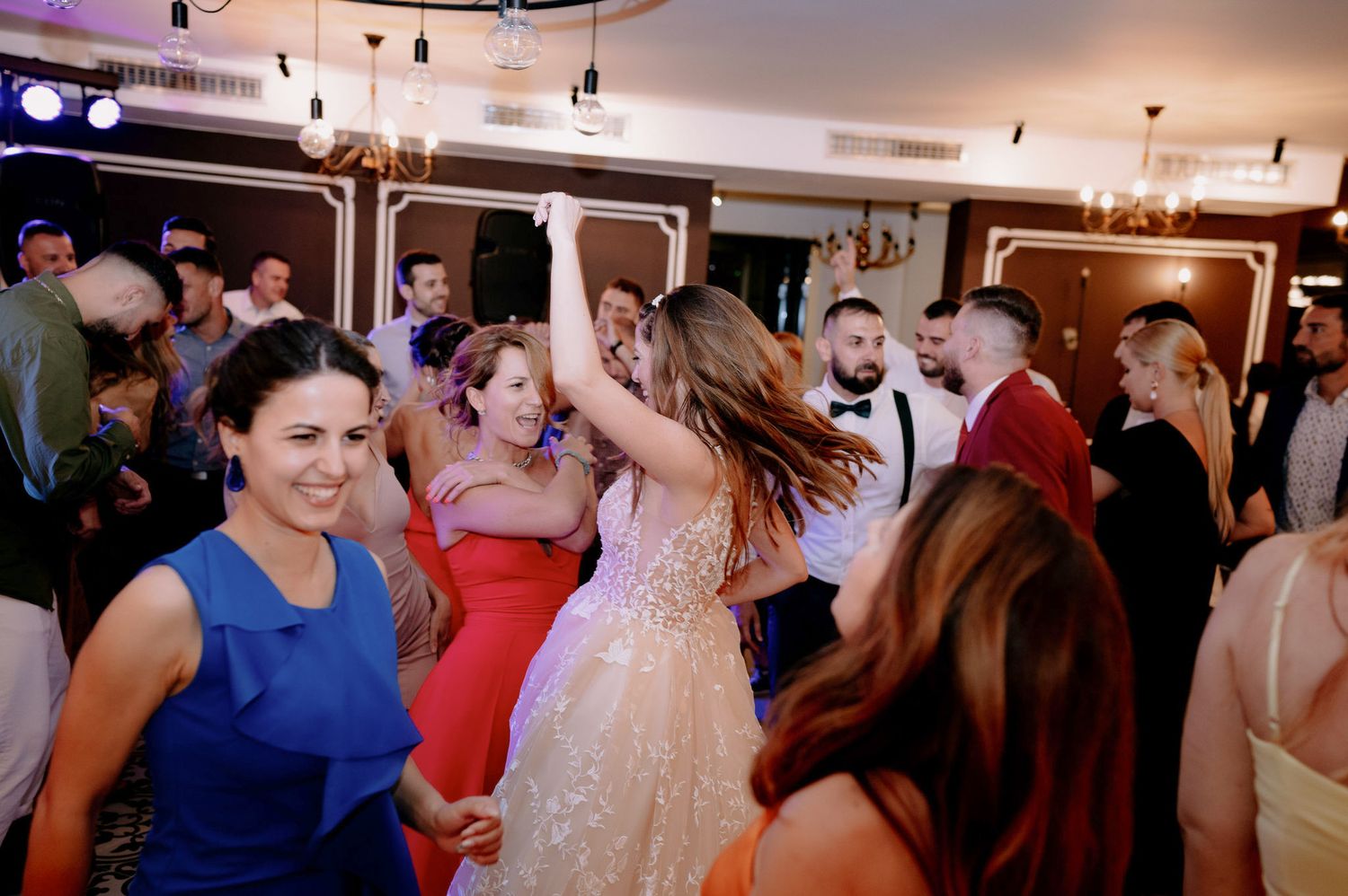 People dancing and celebrating at a wedding reception in a warmly lit indoor venue.