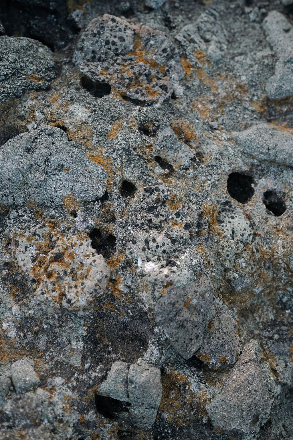 Close-up texture of weathered volcanic rock with porous surface and orange-tinted mineral deposits.
