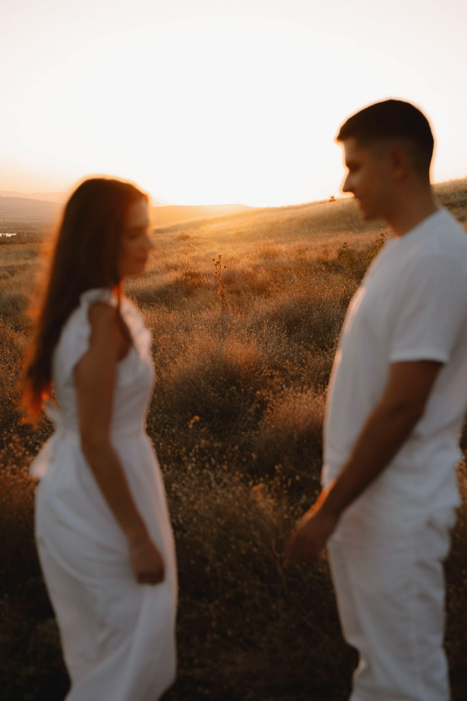 A couple in white outfits embraces during sunset in a field of wildflowers.