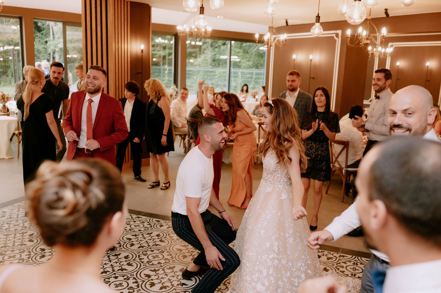 Wedding guests dance and celebrate together on an elegant ballroom dance floor under warm lighting at a reception.