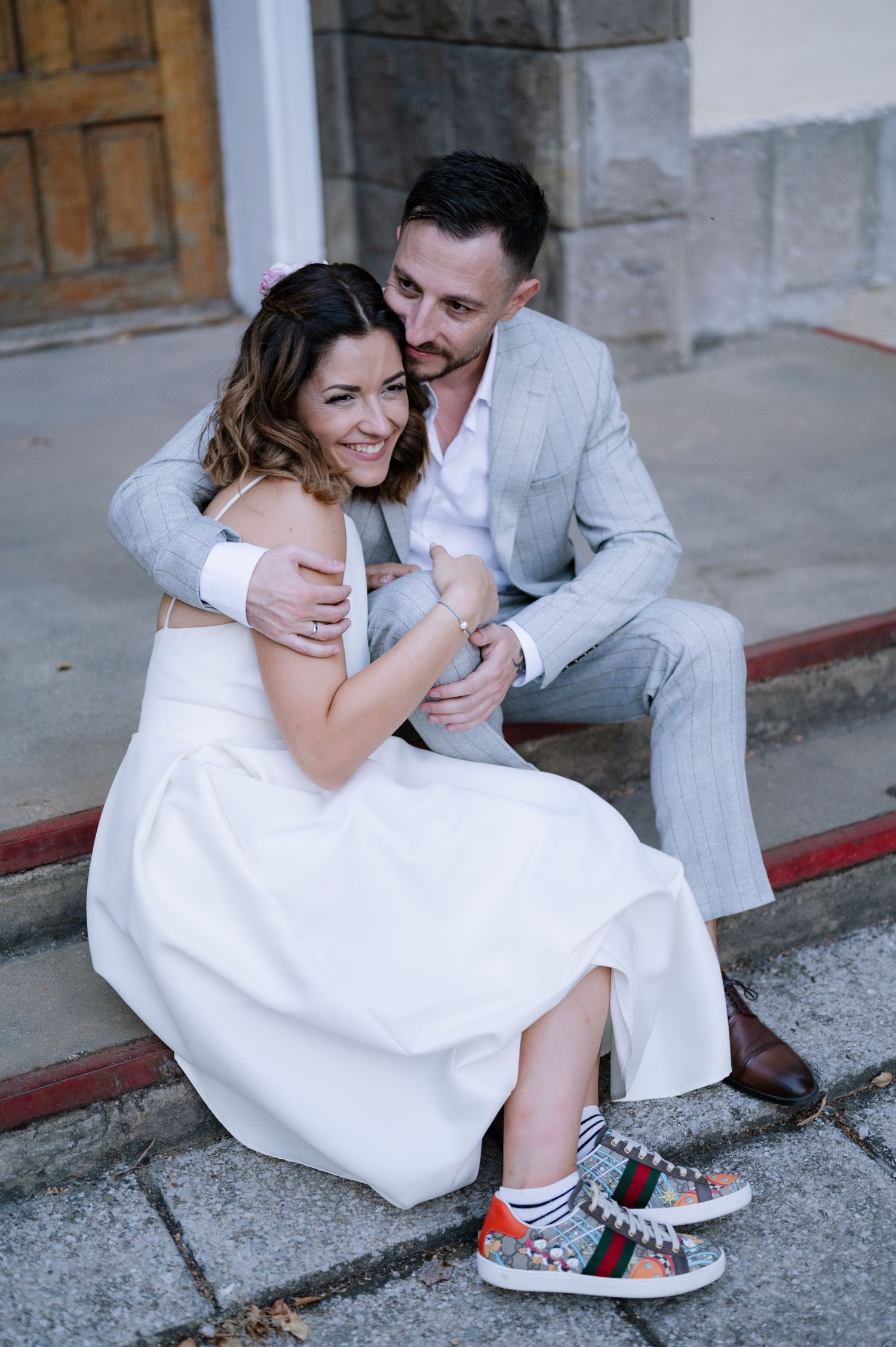 A couple in wedding attire sits on stone steps showing off their colorful sneakers in a series of candid moments.