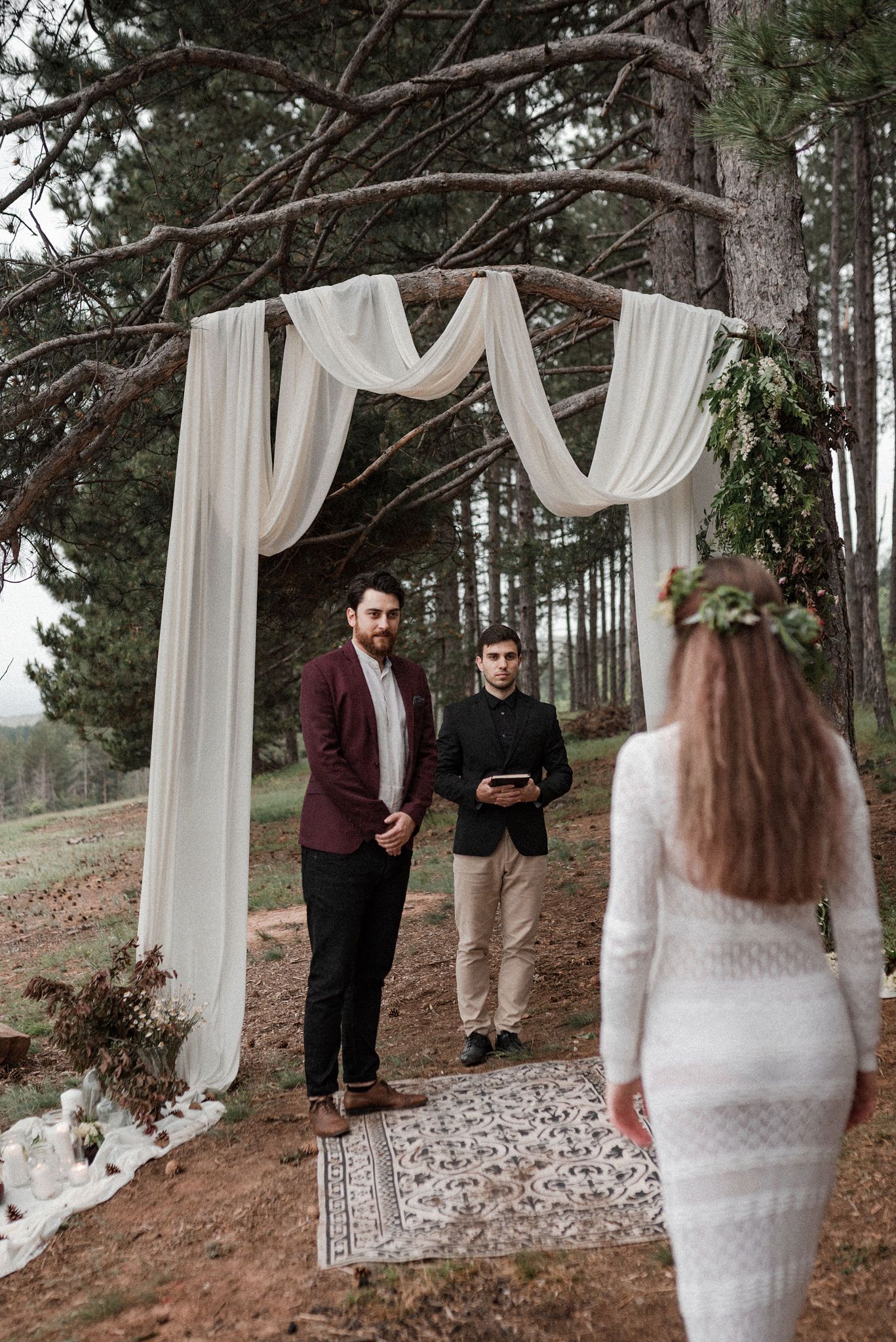 Romantic forest wedding ceremony setup with white fabric draped between trees and a stone-covered aisle path.