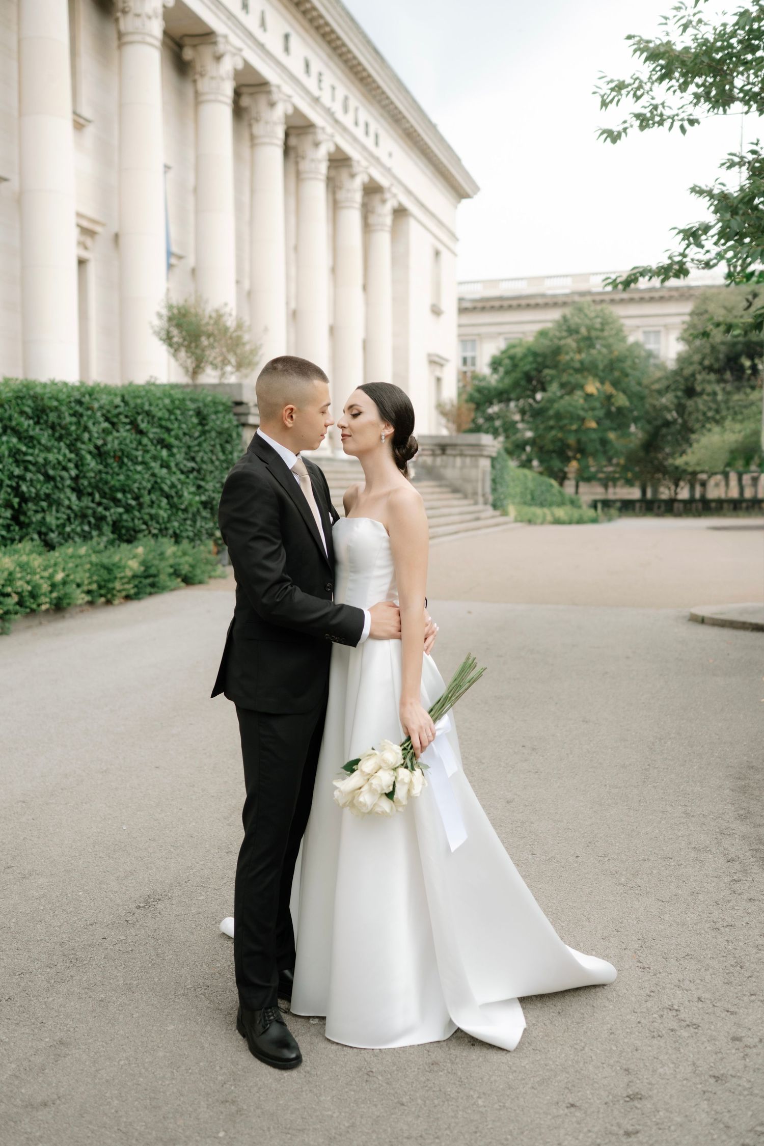 A romantic wedding portrait series showing tender moments between newlyweds by a historic colonnade.