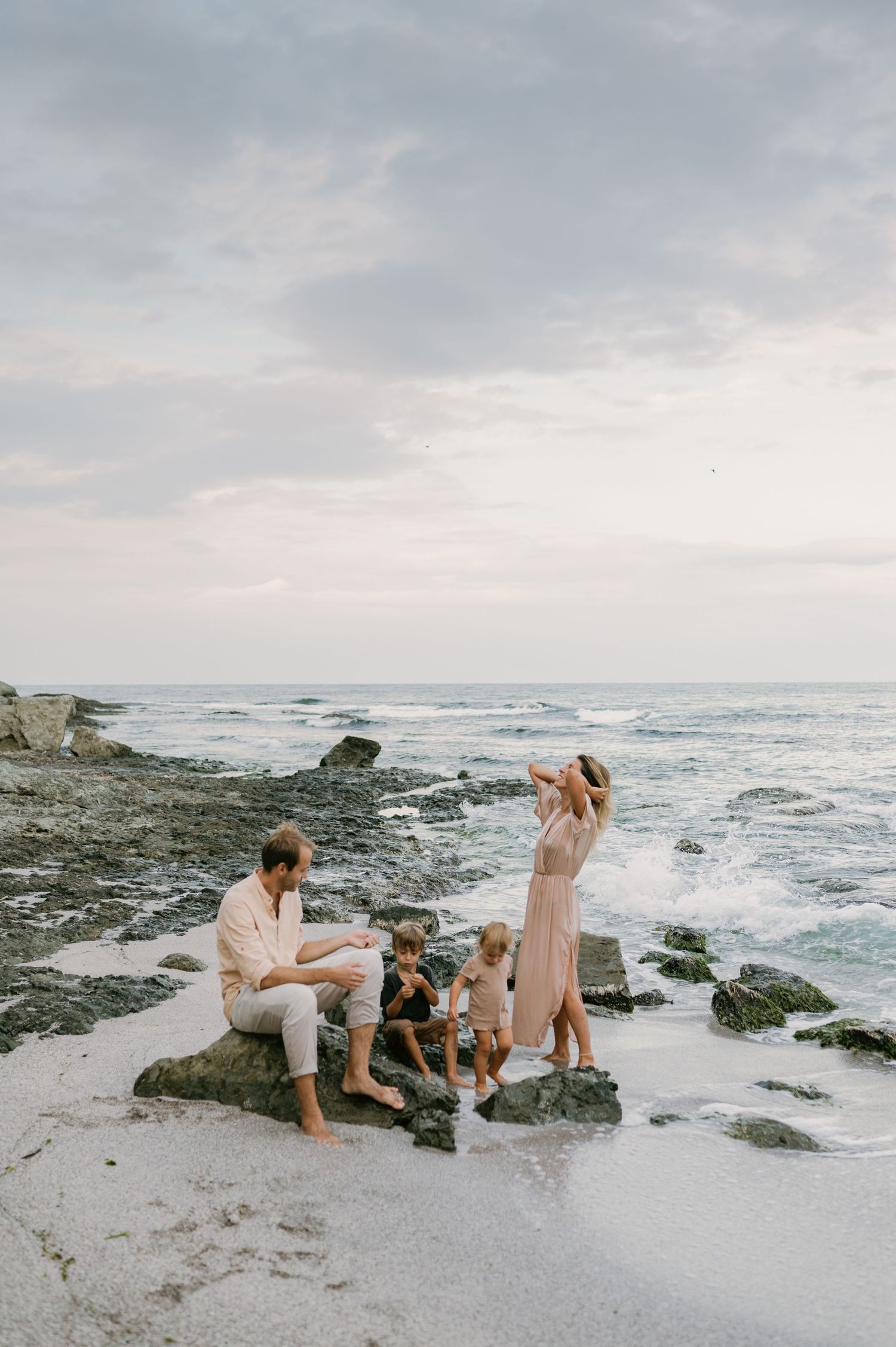 Family of four enjoying a serene beach sunset, with waves crashing on rocky shores.