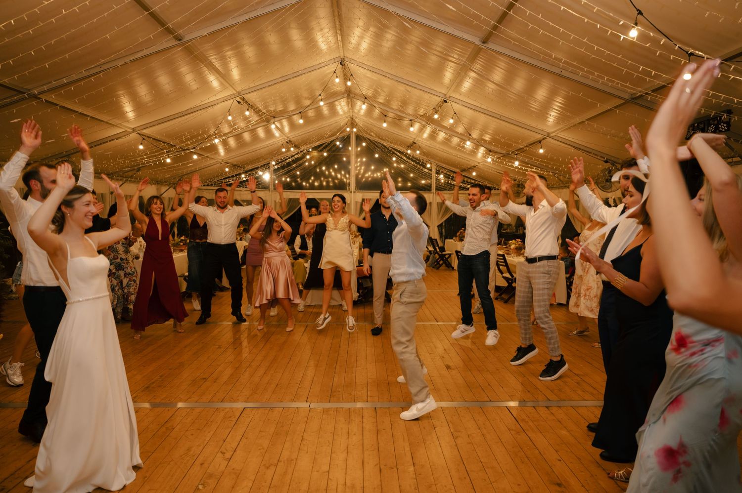 Wedding guests dancing and celebrating under string lights in a rustic barn reception venue.