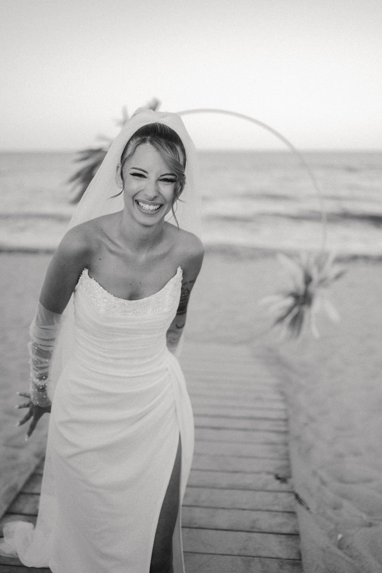 A sequence of black and white photos showing a person in a white dress walking along a wooden boardwalk at the beach.
