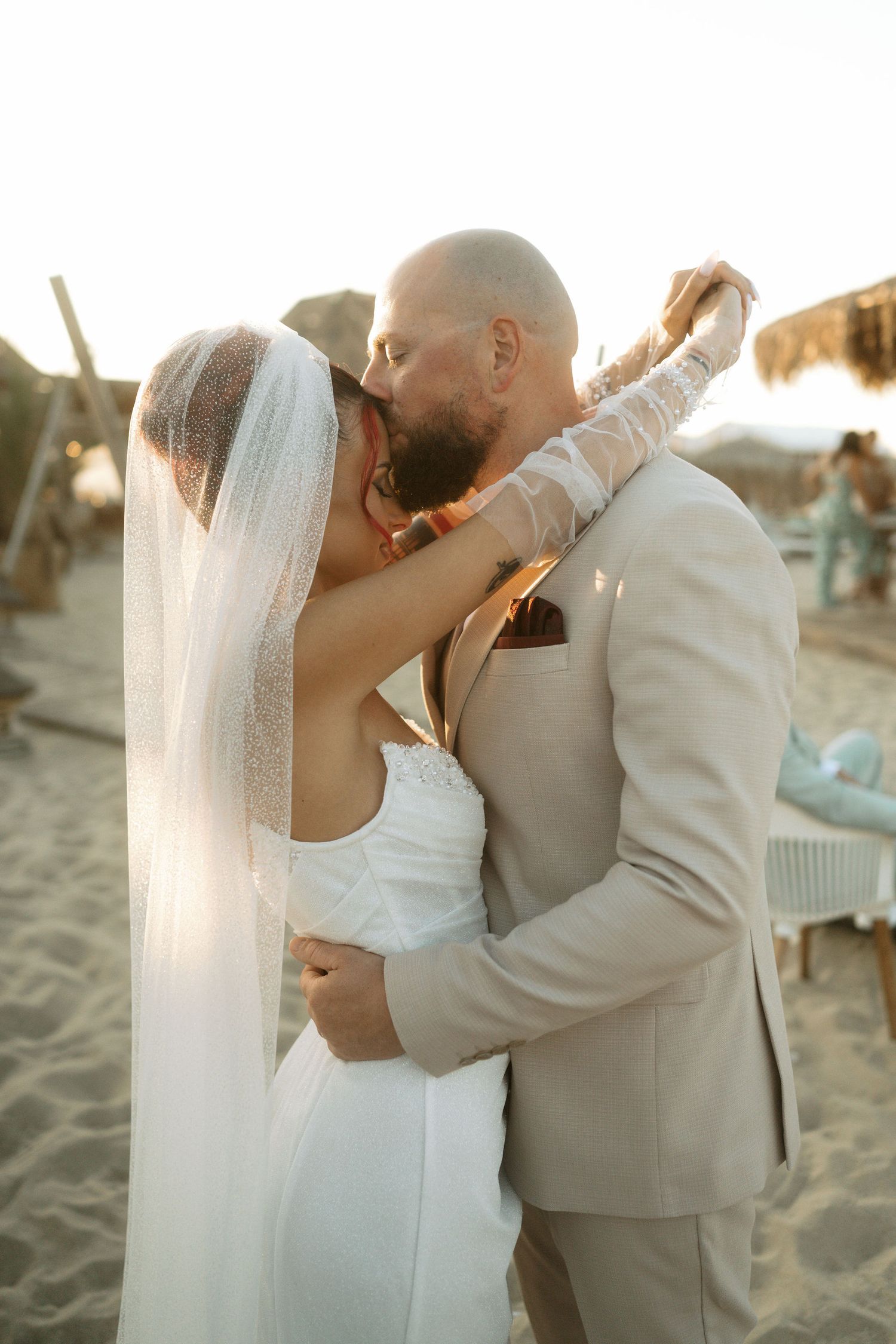 A romantic beach wedding scene shows a couple sharing a kiss at sunset while wearing a white dress and beige suit.