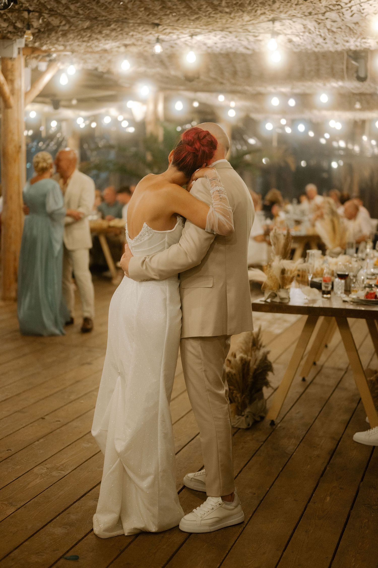 Wedding couple shares intimate dance on rustic wooden deck under romantic string lights at evening reception.