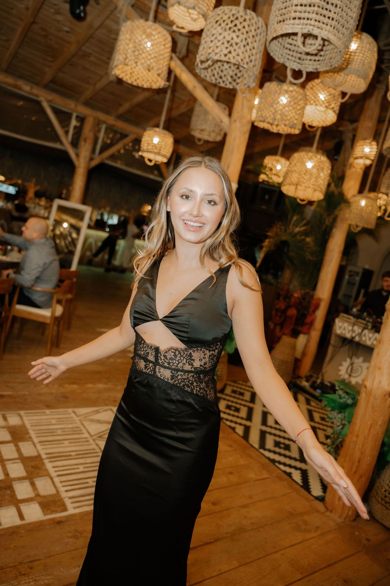 Woman in black lace top dancing under rustic chandelier lighting at an evening event venue.