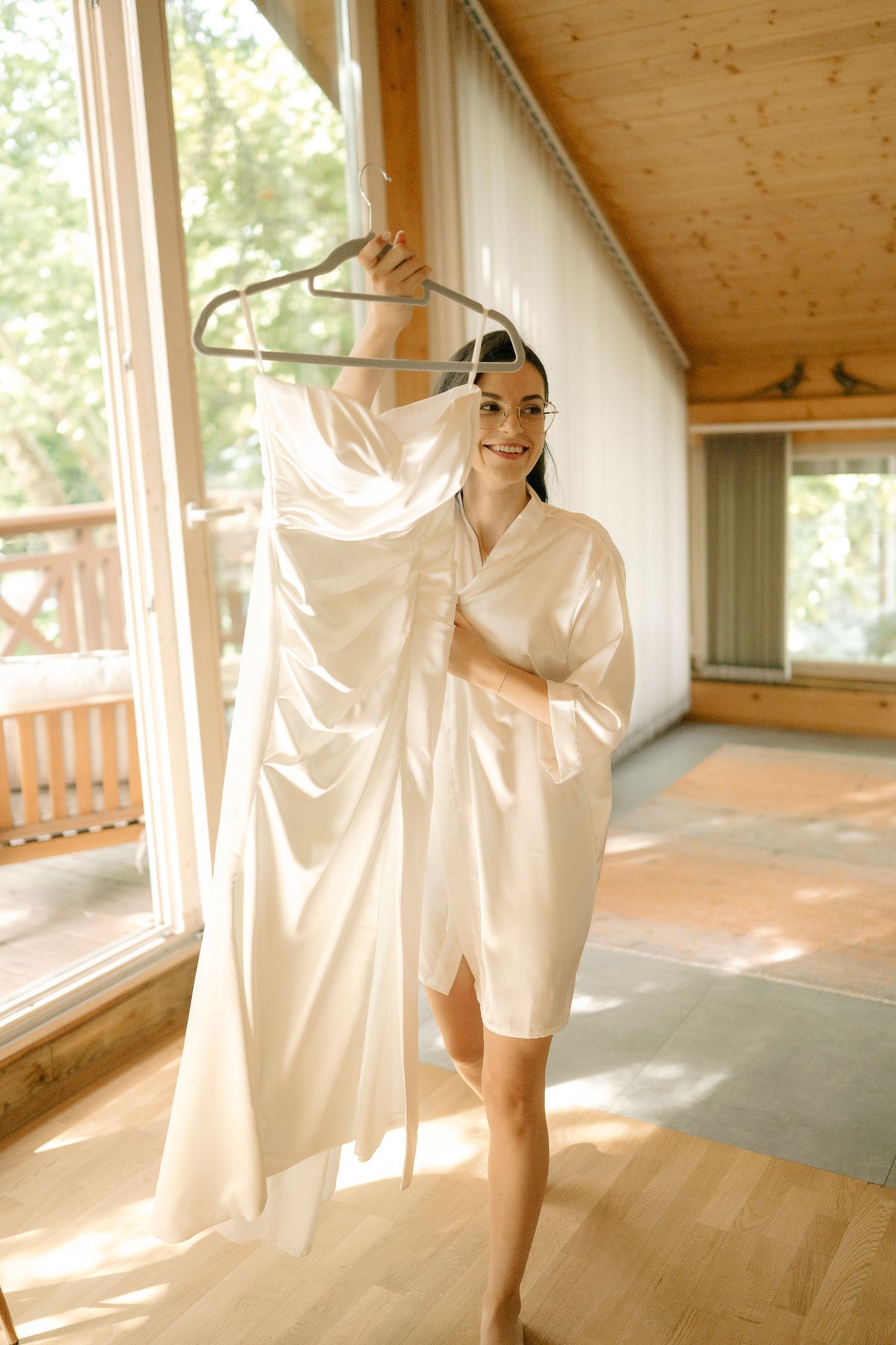 White curtains billow in sunlight against wooden walls and windows in a minimalist interior space.