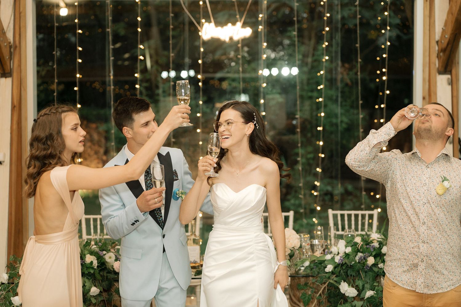 Wedding party guests dance and celebrate together in a dimly lit reception venue with twinkling lights in the background.
