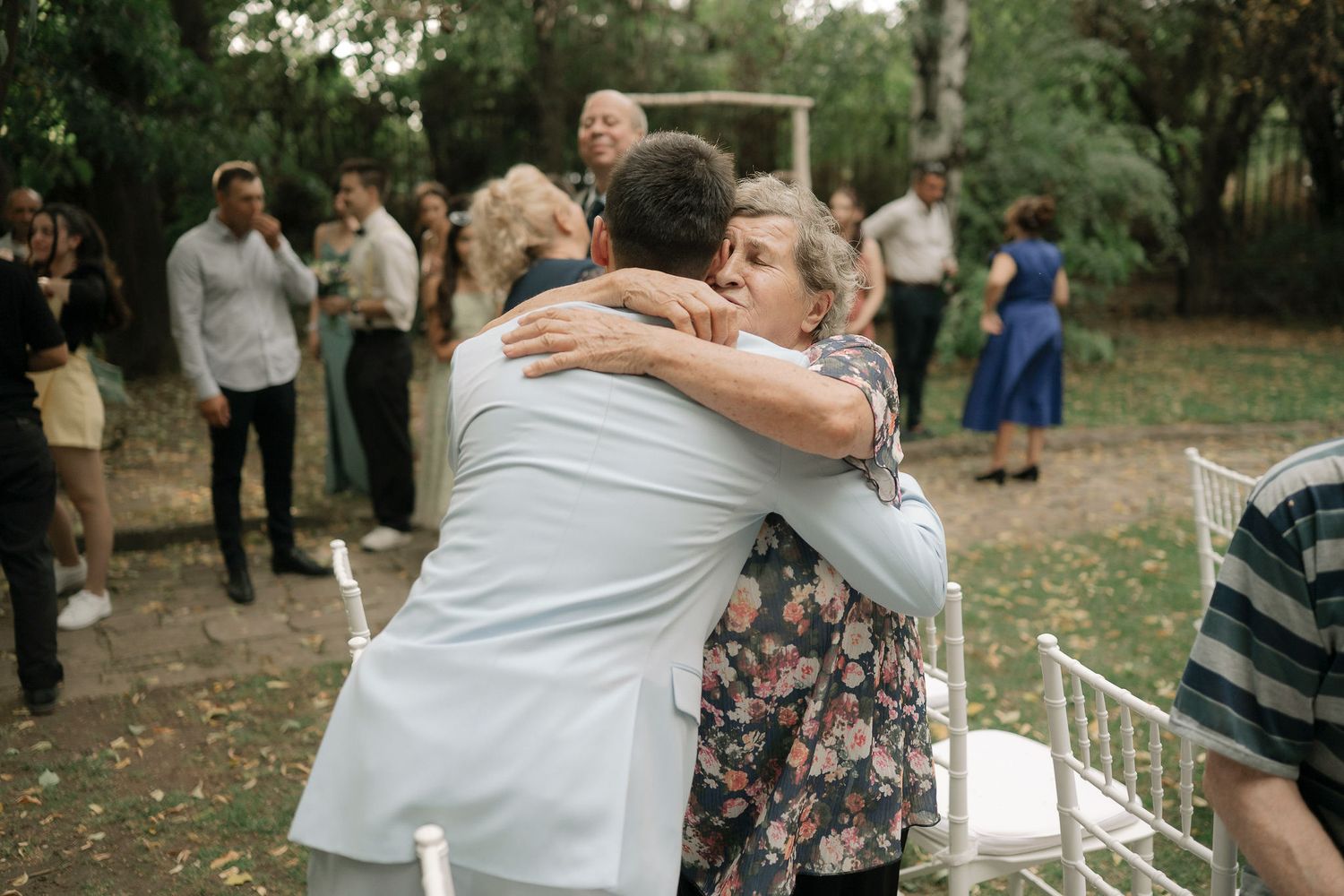 Two people embrace in a tender moment during an outdoor celebration in a park setting.
