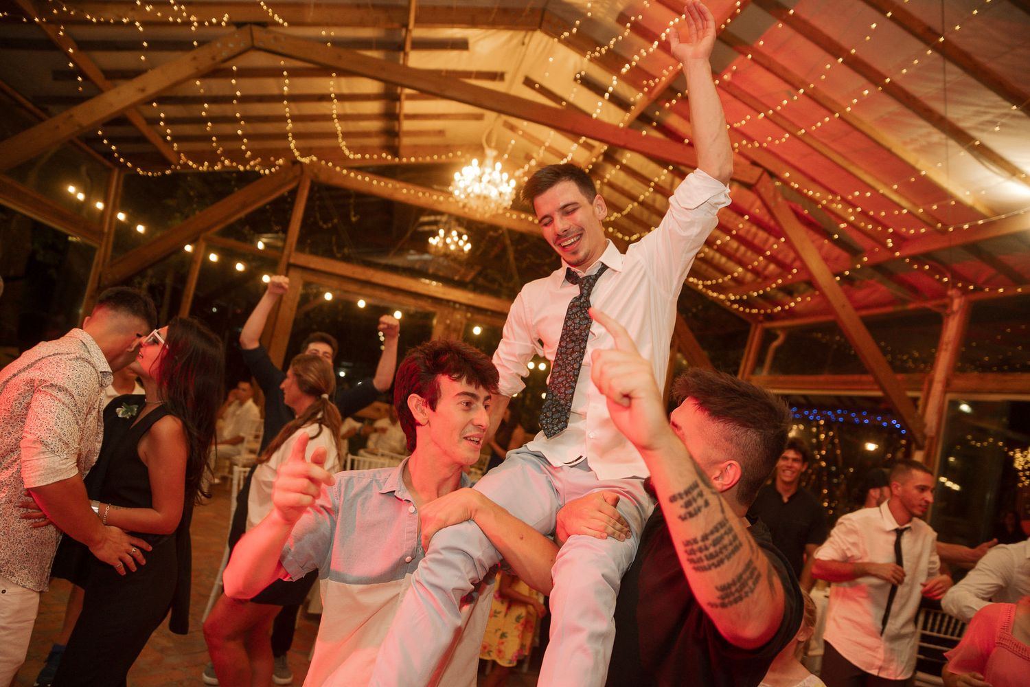 Energetic dancing and celebration at a wedding reception under warm lighting and string lights.