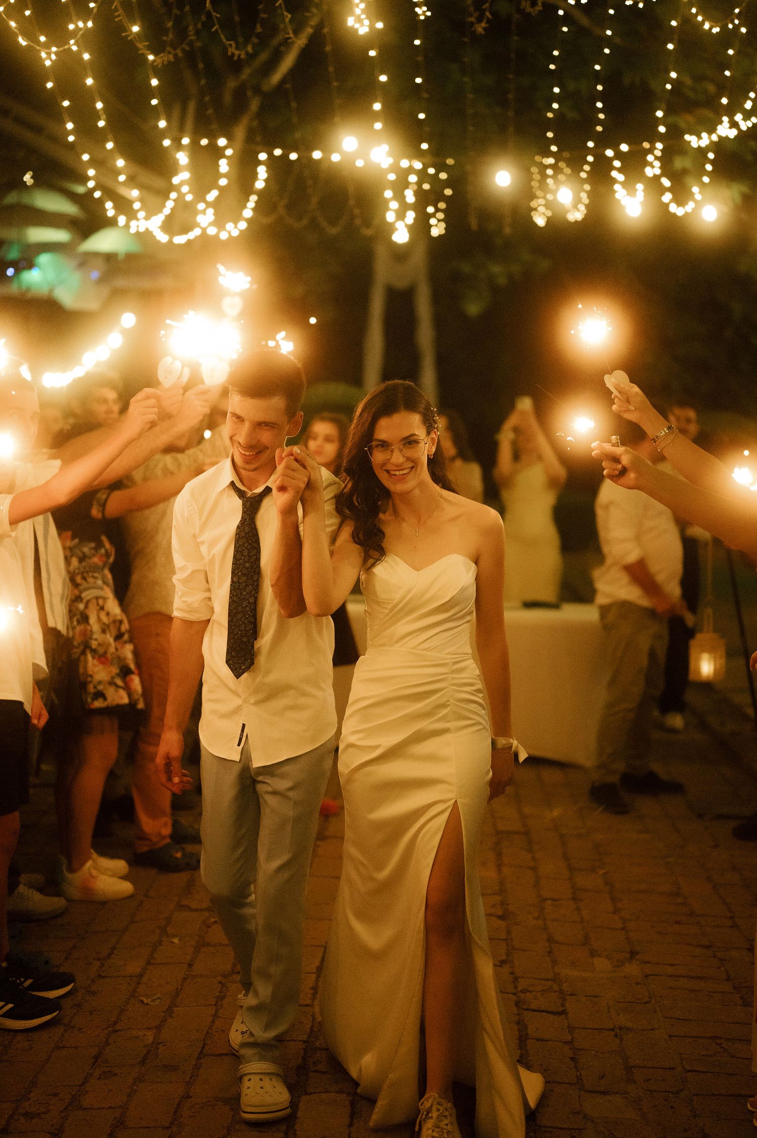 A romantic evening wedding reception with couples dancing under twinkling string lights on a brick patio.