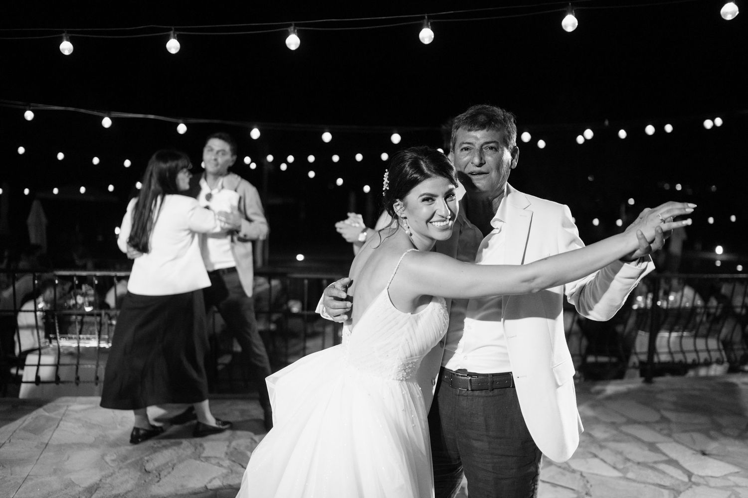 Dancers move gracefully on an outdoor dance floor under twinkling string lights at a nighttime celebration.