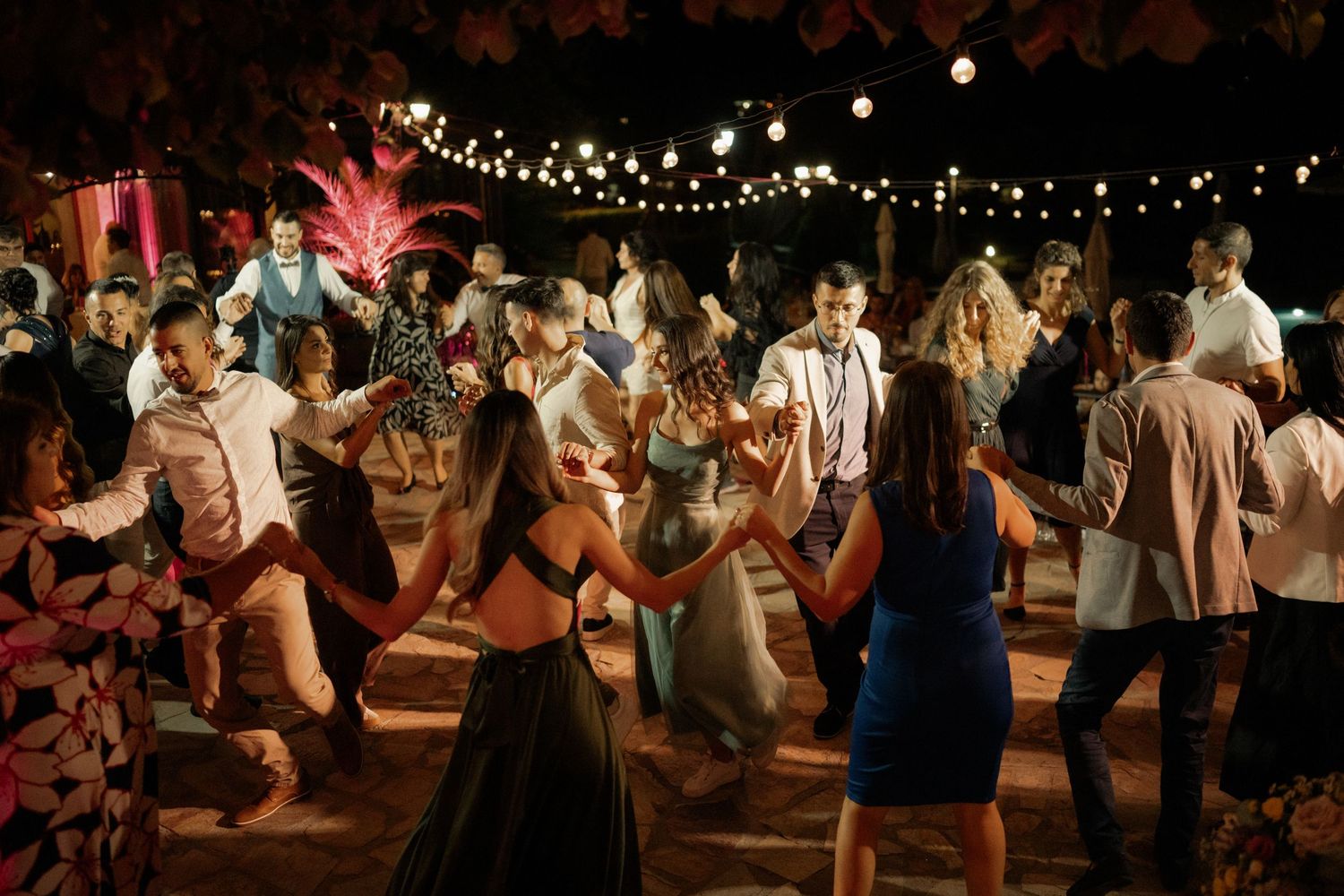 People dancing at a rustic wedding reception under string lights and wooden beams in a barn venue.