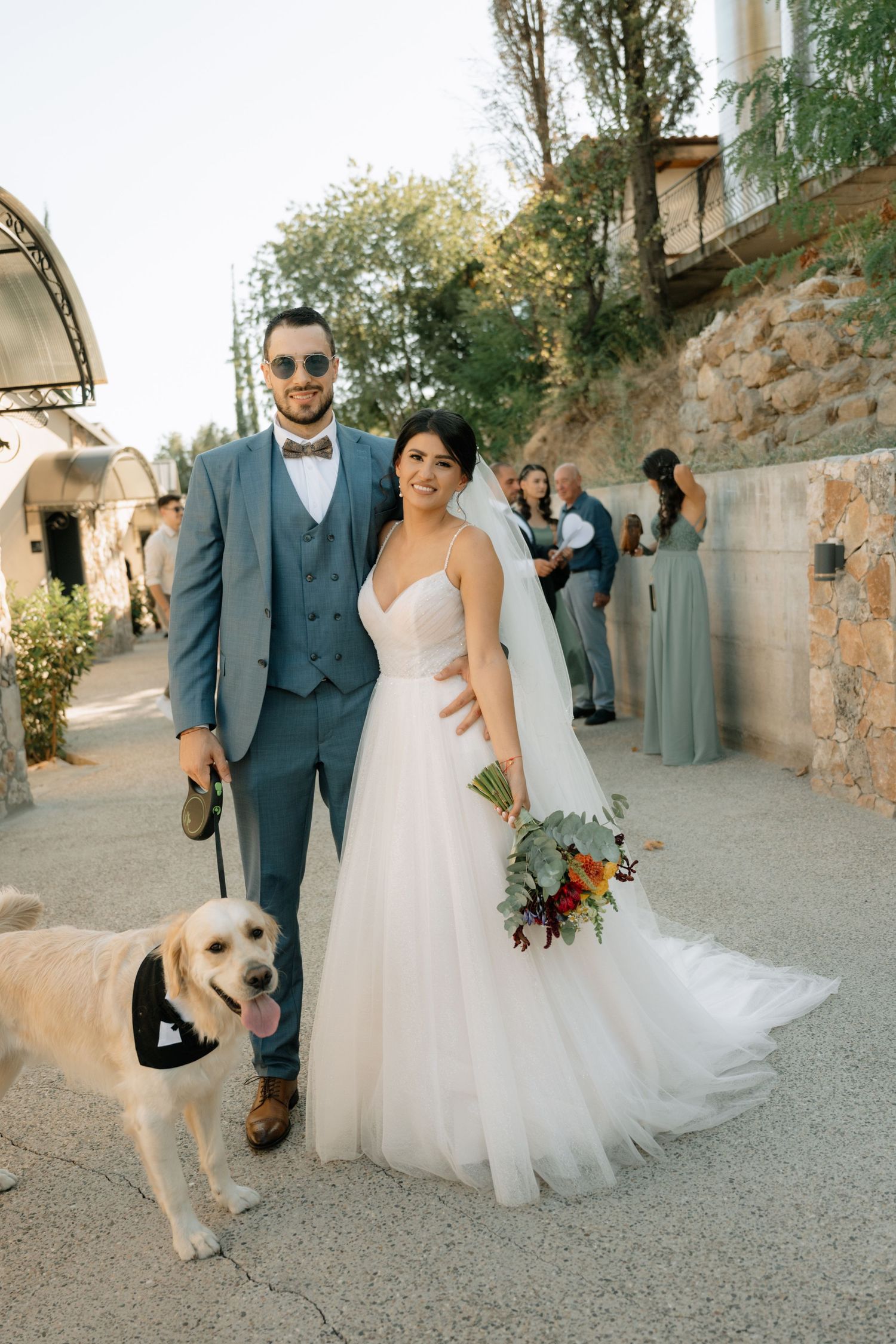 A couple in wedding attire poses with their golden retriever on a rustic stone path during their special day.
