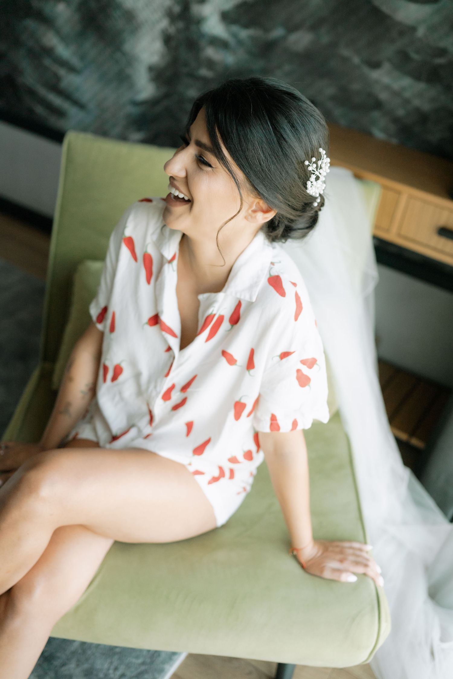 Woman in white dress with red heart pattern lounges on mint green couch in soft lighting.