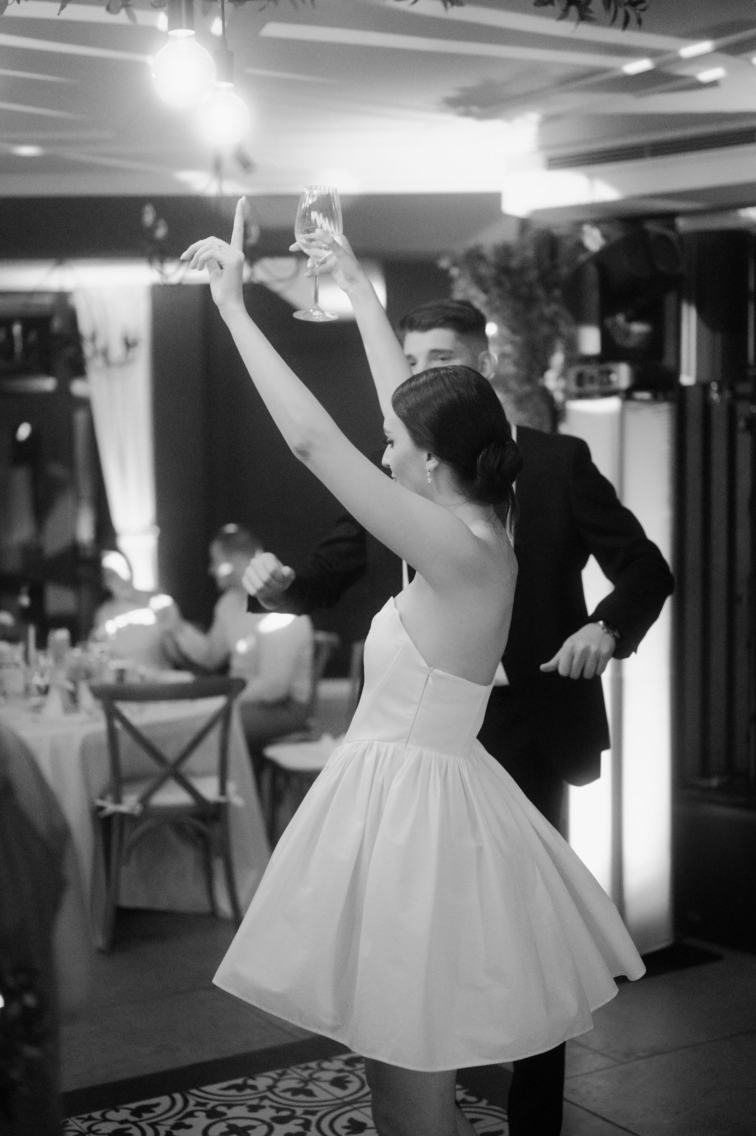 A couple dances at a wedding reception, with the bride wearing a short white strapless dress in black and white photography.