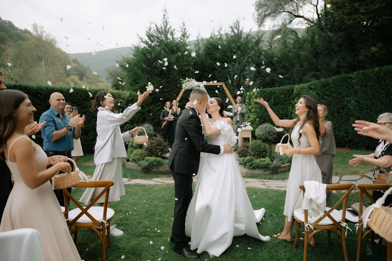 A group of people dancing and celebrating outdoors at a rustic wedding reception with wooden tables and chairs.