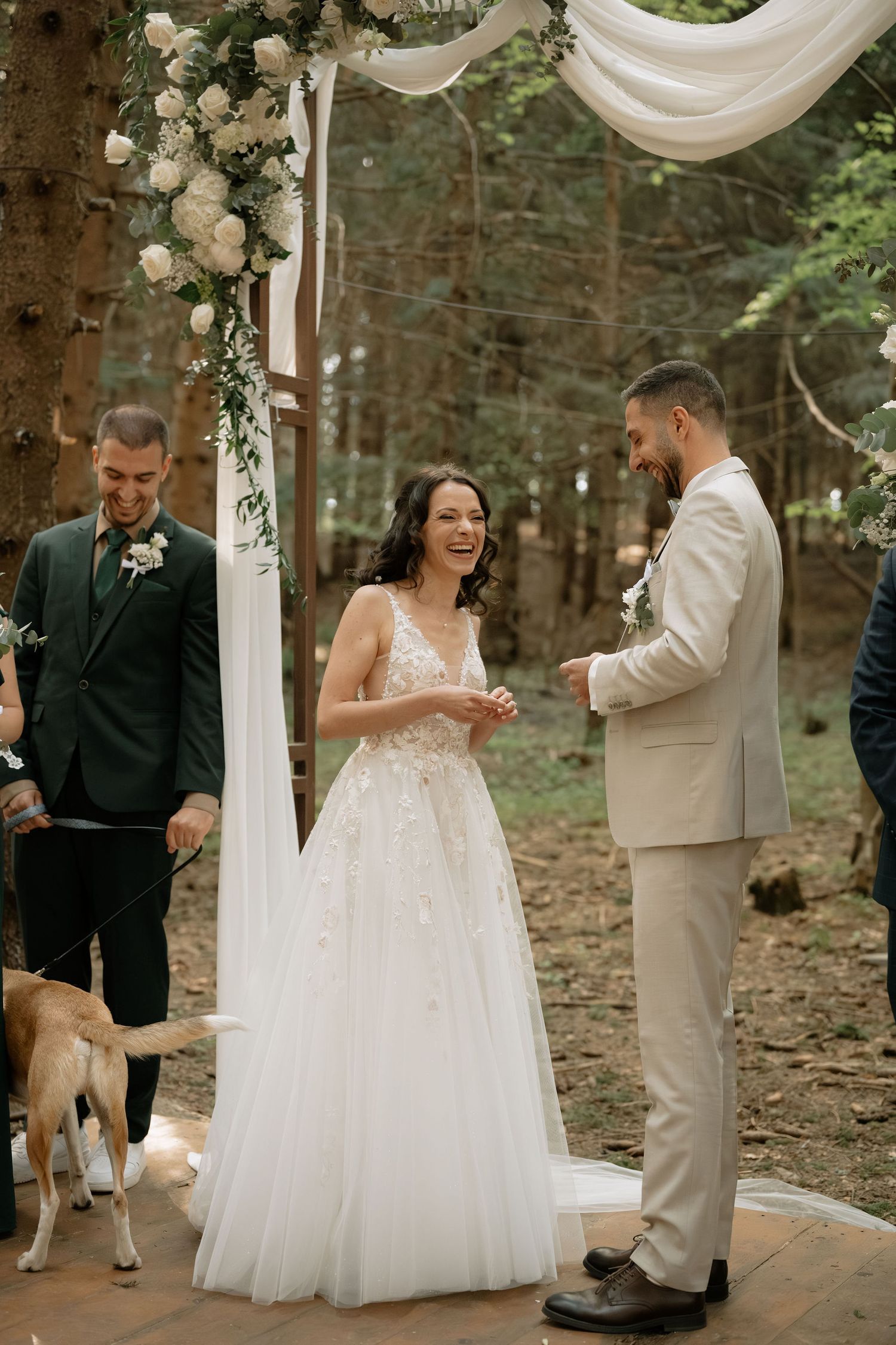 Bride and groom exchanging vows outdoors under a floral arch in a forest wedding ceremony.