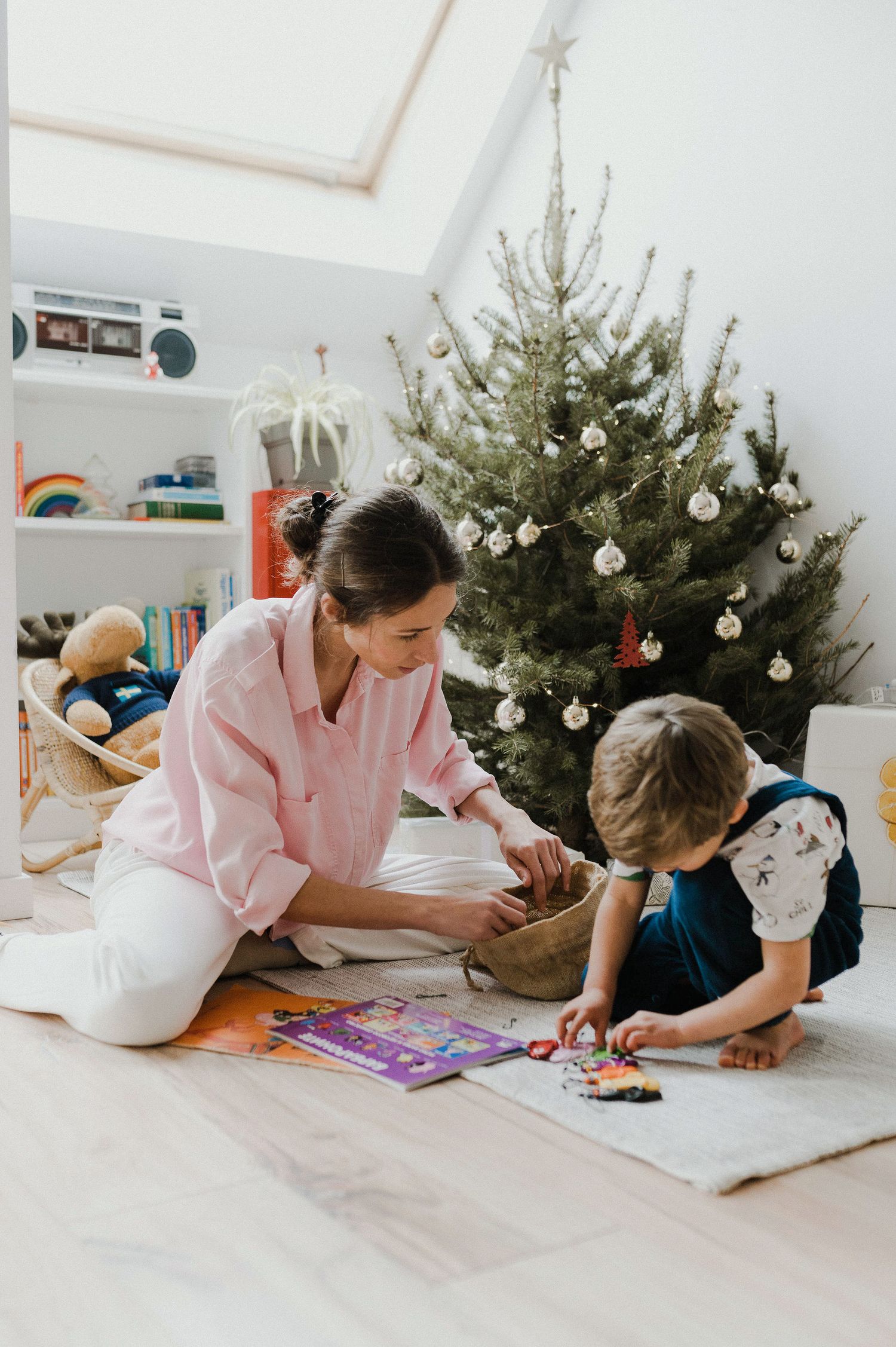 Parent and child lying on floor doing arts and crafts activities together near decorated Christmas tree.