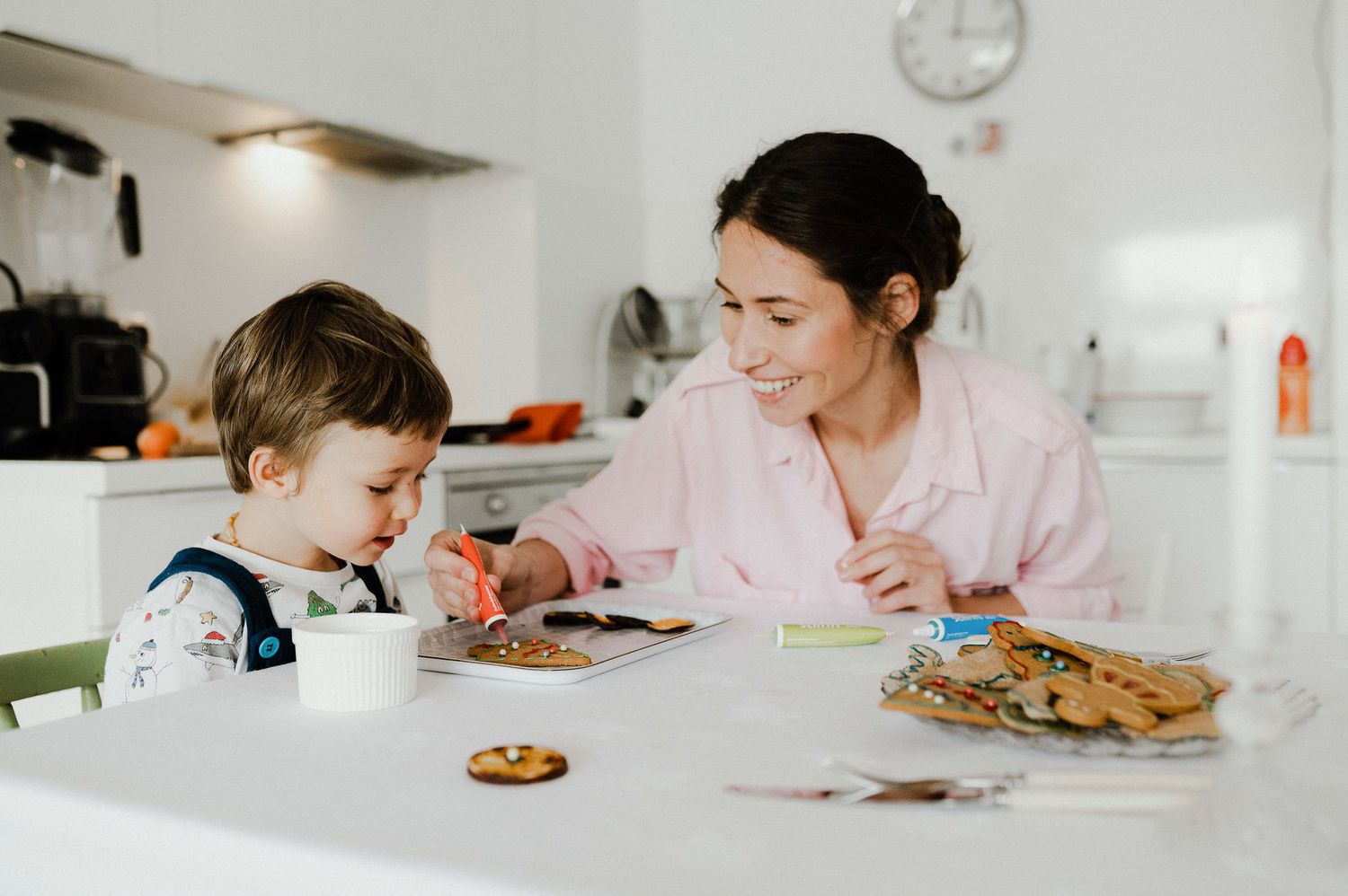 Two people sit at a kitchen counter enjoying chocolate chip cookies and milk together.