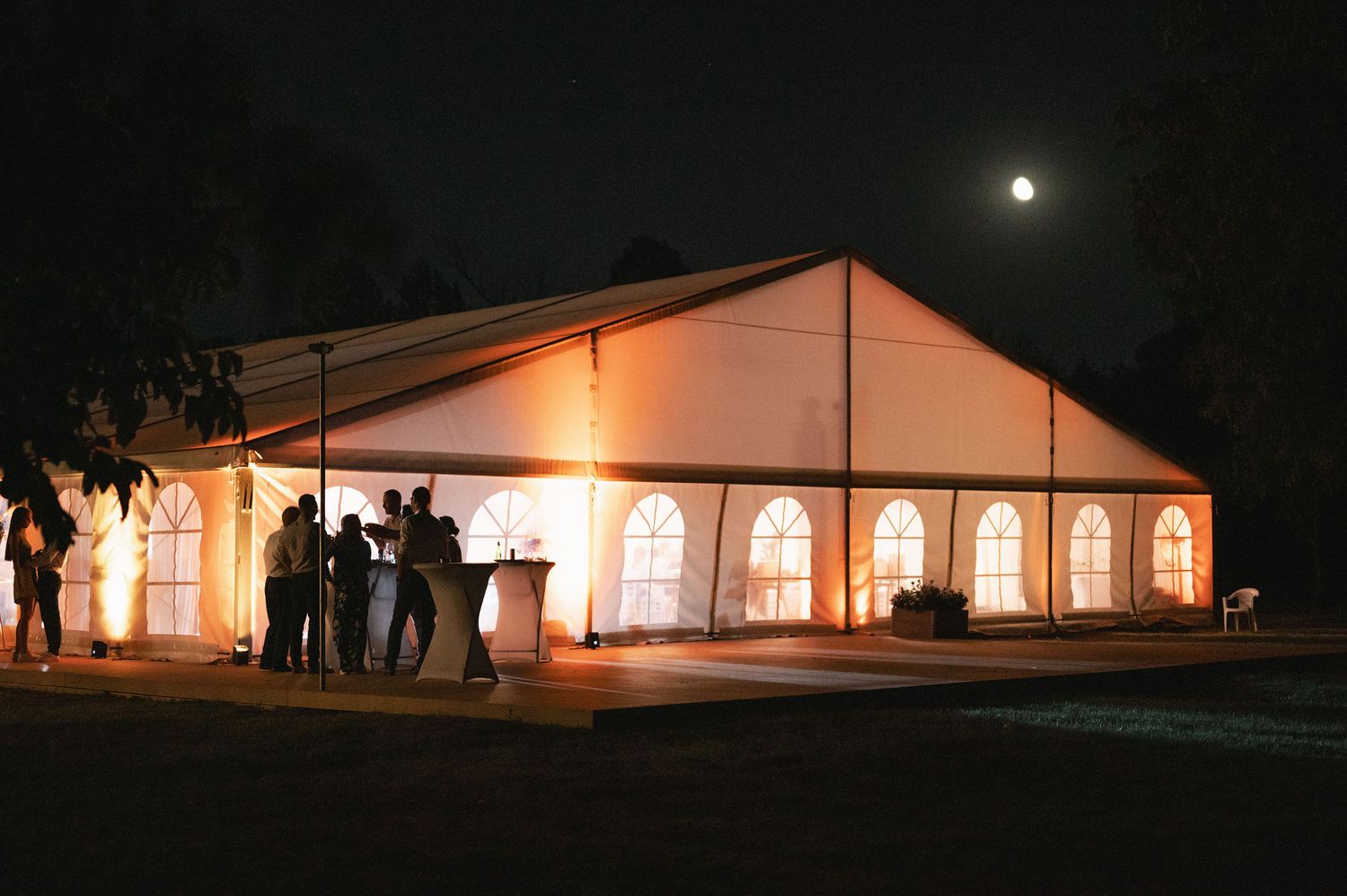 Large white wedding tent illuminated at night with warm glowing lights creating a romantic outdoor atmosphere.