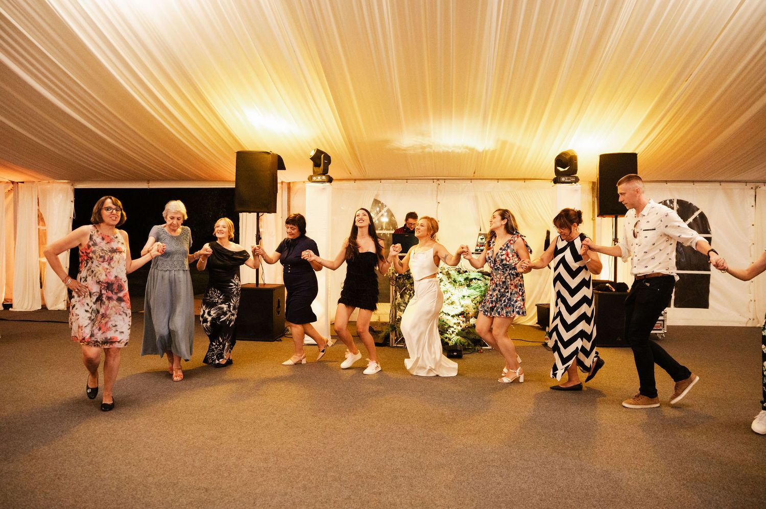 Panoramic view of a wedding reception dance floor with guests dancing and celebrating in a white-decorated venue.