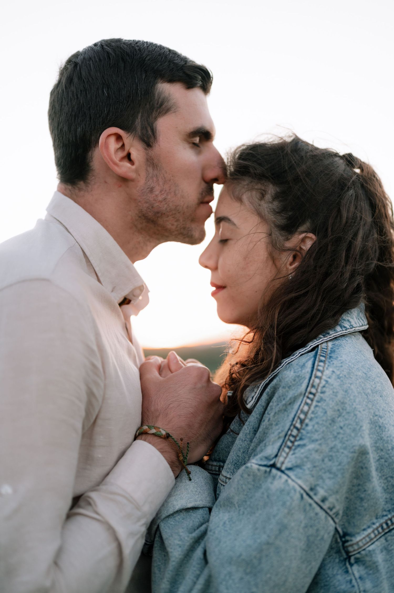 Couple in denim jacket embracing tenderly against golden sunlight backdrop.