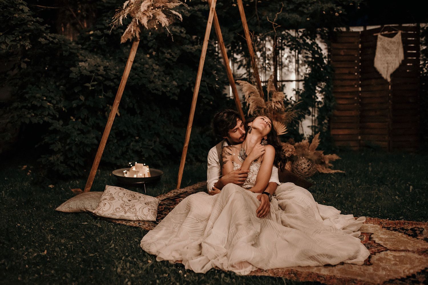 A couple in wedding attire sits together on a swing in a romantic garden setting with warm moody lighting.