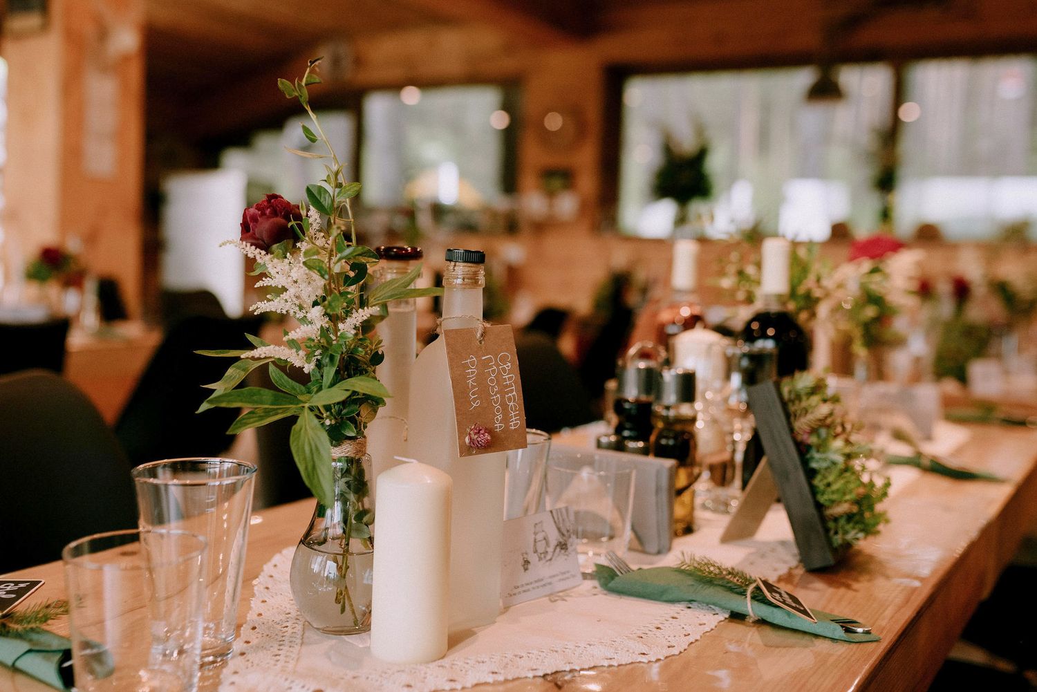 Elegant table settings with white candles and greenery on wooden tables at a rustic venue.