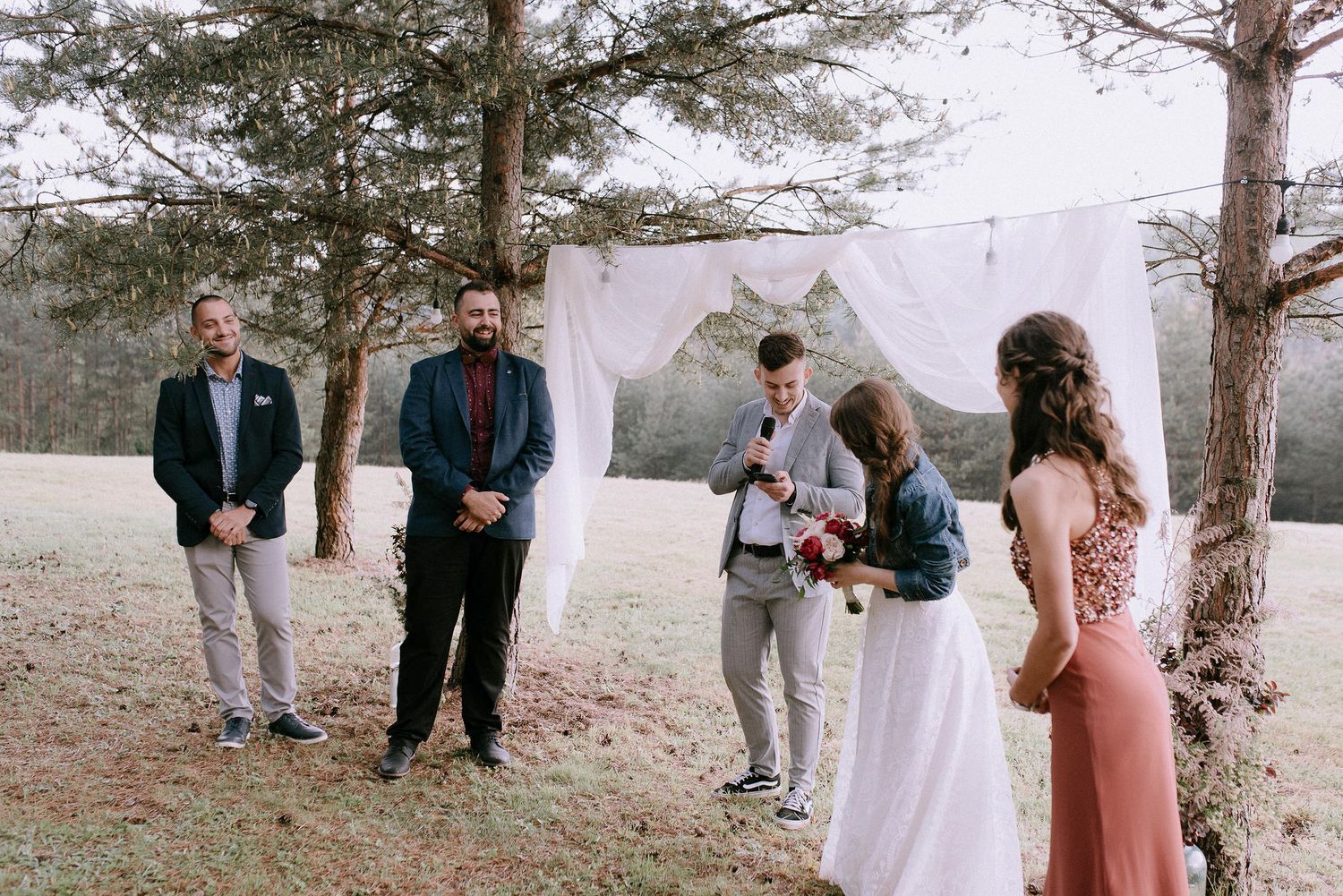 Intimate outdoor wedding ceremony with guests gathered among tall pine trees.