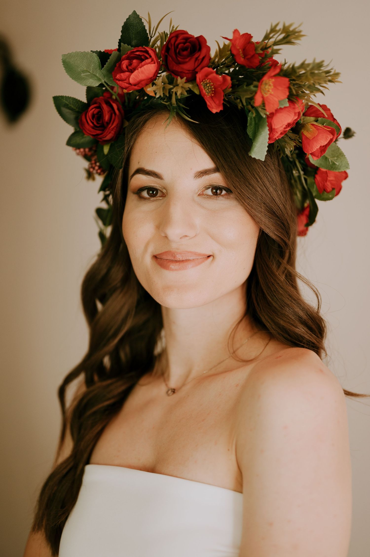 Romantic bridal portrait featuring white gown and vibrant red rose crown against beige backdrop.