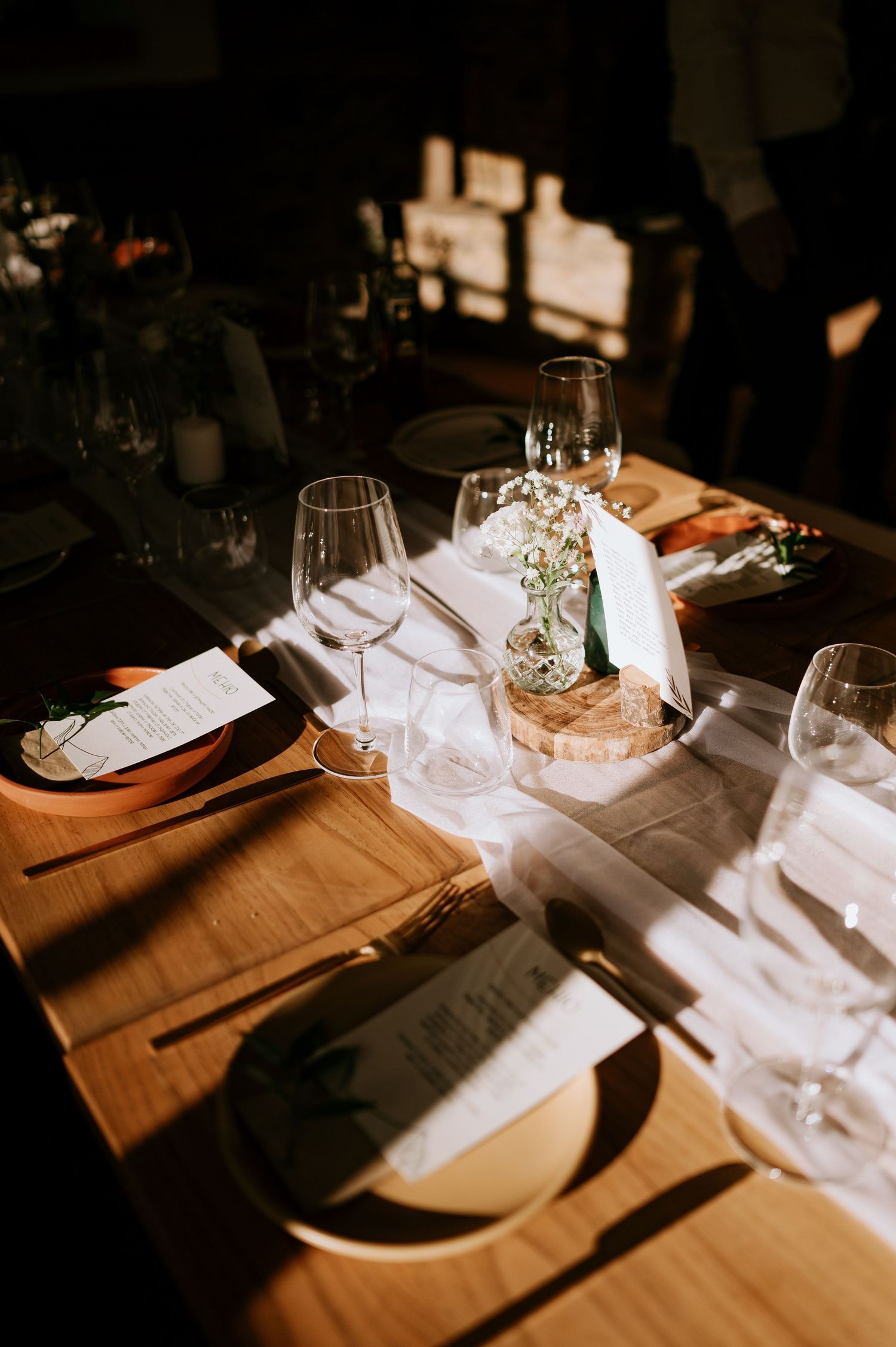 Moody dining table setup with wine glasses and place settings in dramatic lighting.