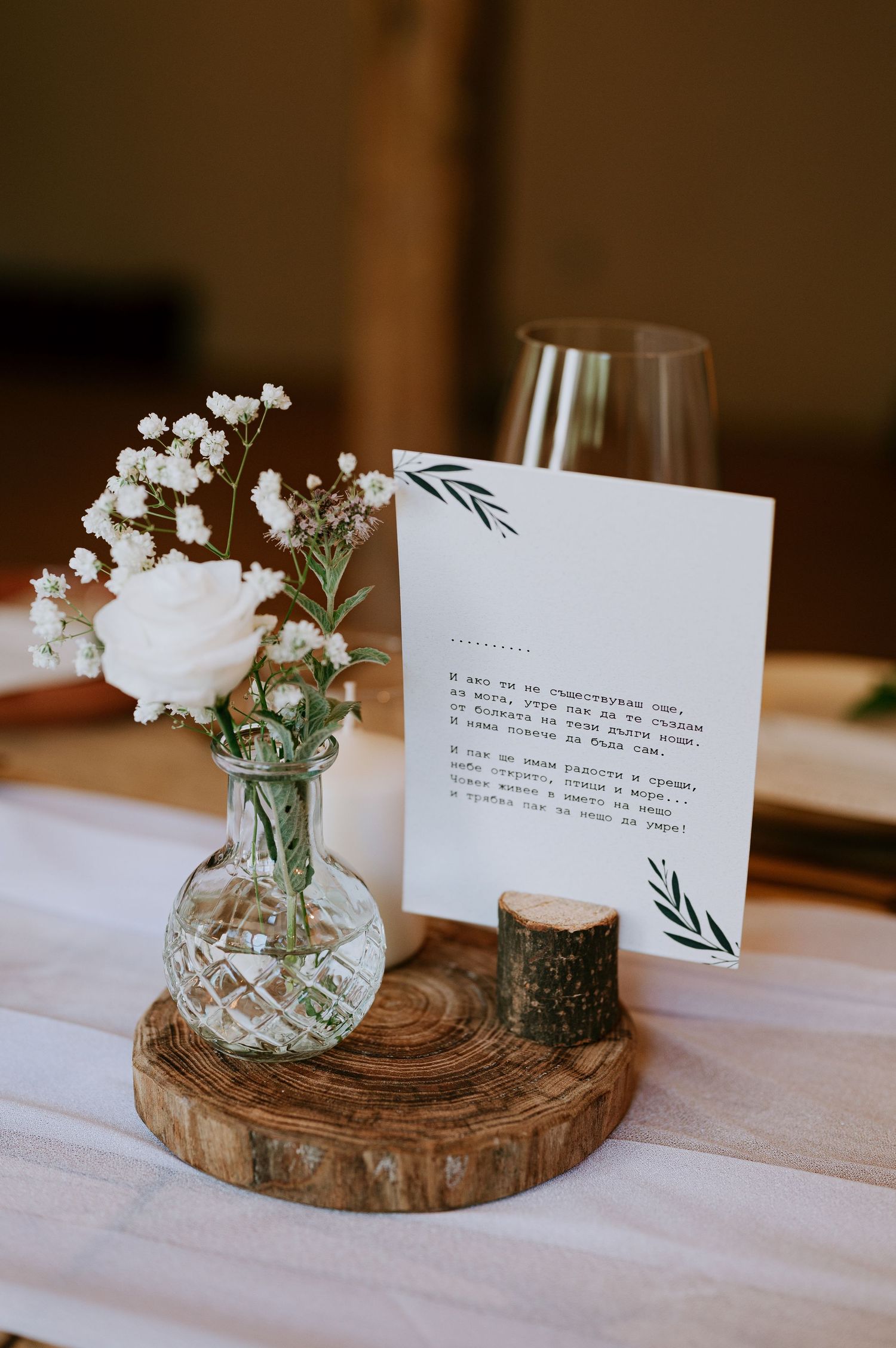 White rose and baby's breath centerpiece with menu card on rustic wood slice and green candle.