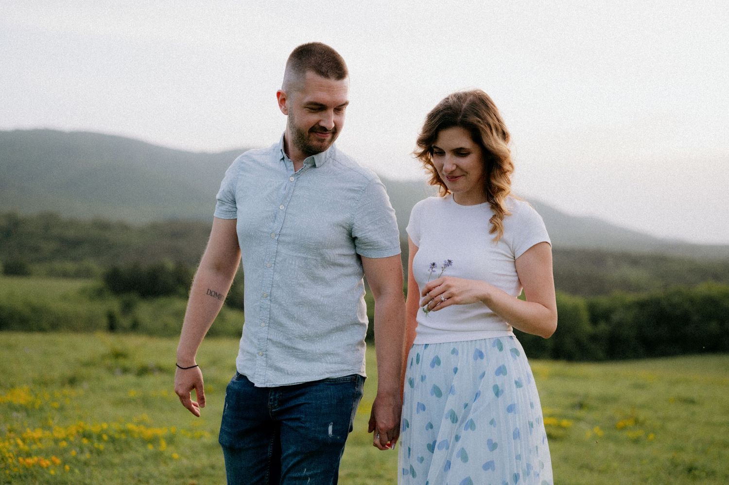 Couple walking through mountain meadow with wildflowers and scenic mountain views.