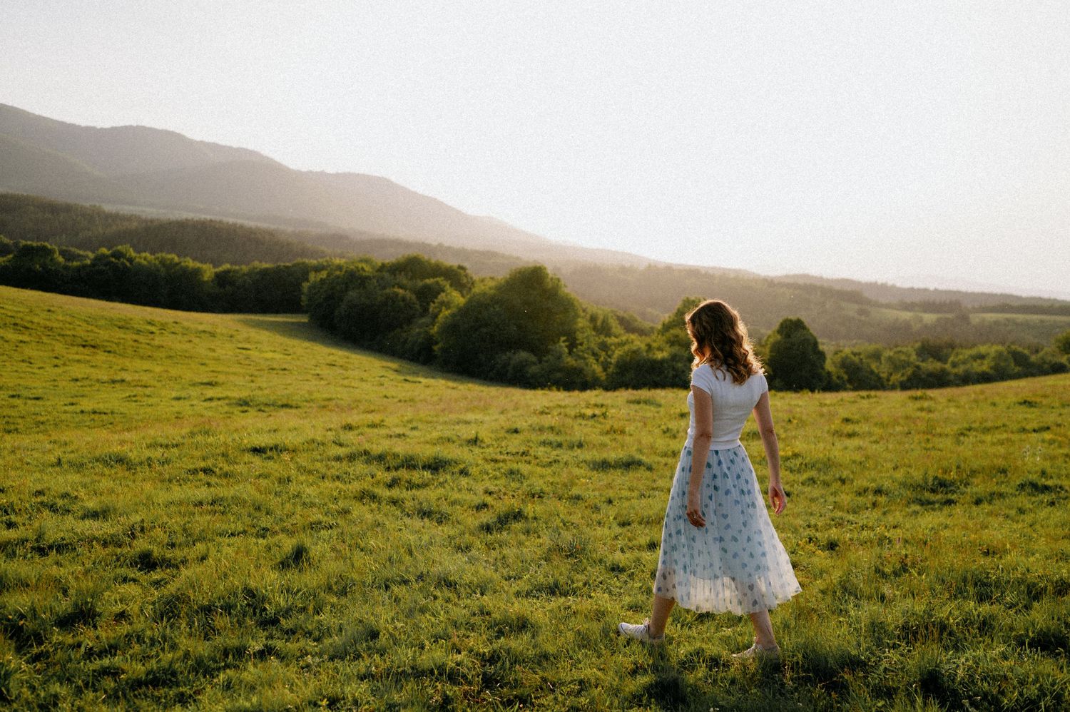 A dreamy scene of someone spinning in a white dress against rolling hills at dusk.