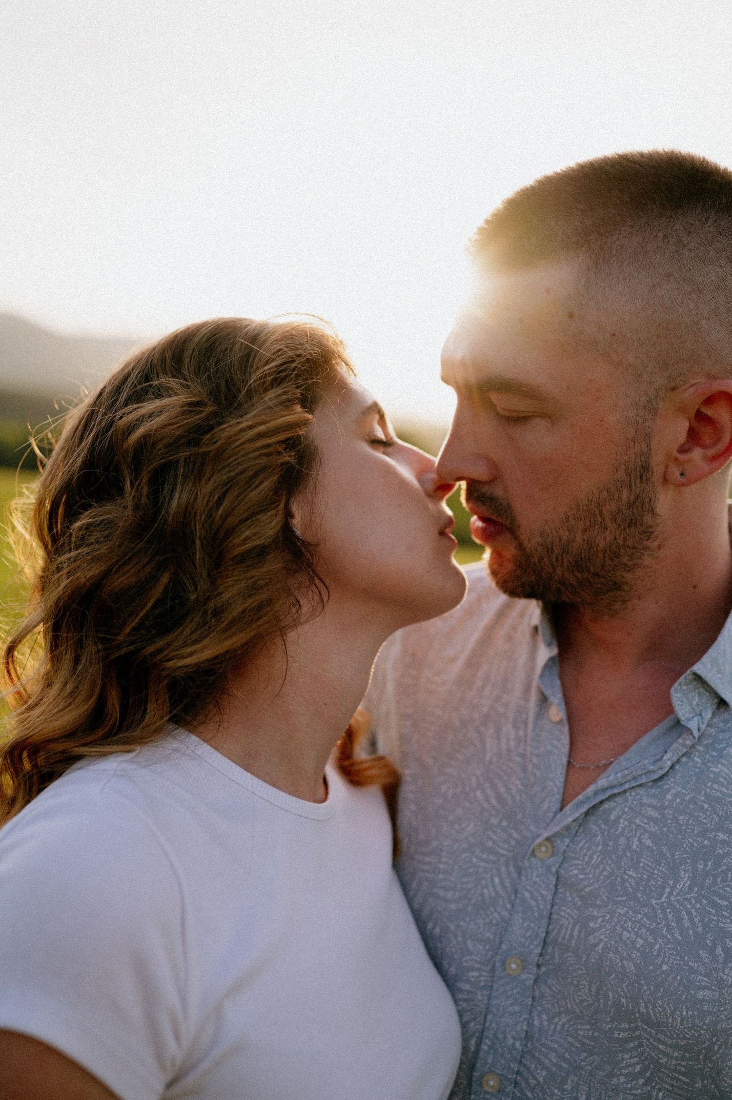 A couple shares a kiss in a meadow during golden hour.