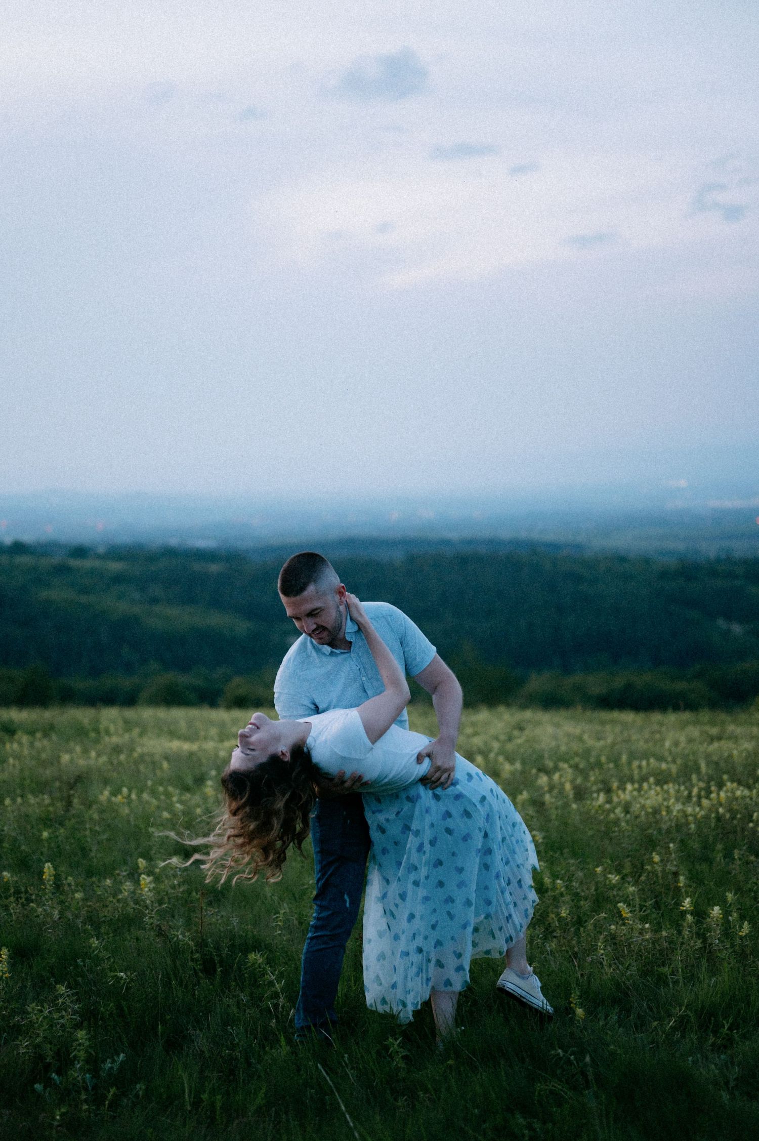 A romantic dip dance pose in a hilltop meadow during blue hour.