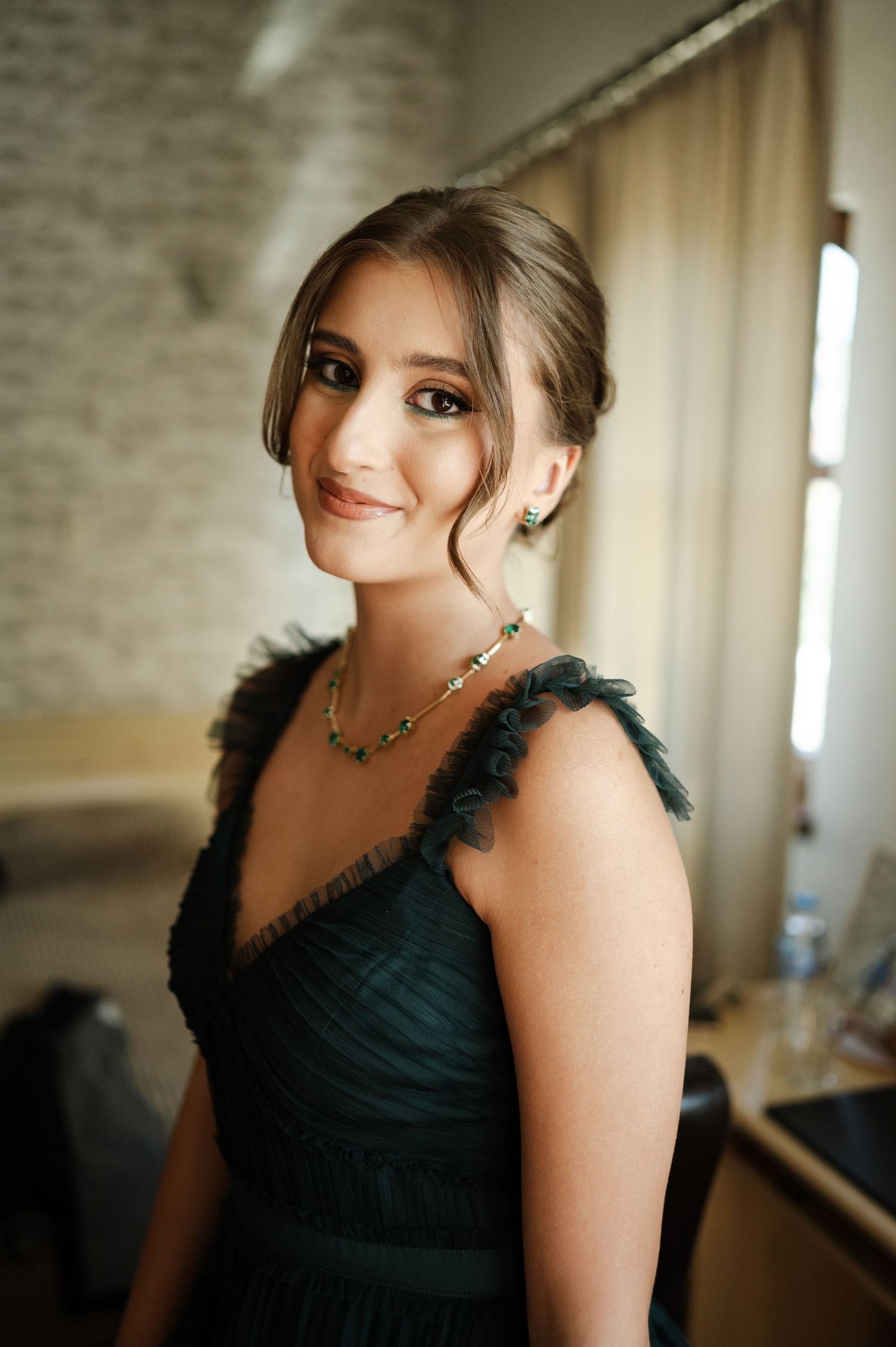 Bridesmaid wearing an elegant black dress with feather details in a softly lit room.