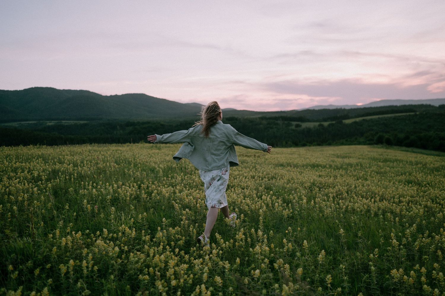Figures twirl joyfully in a golden meadow against a dusky mountain landscape.