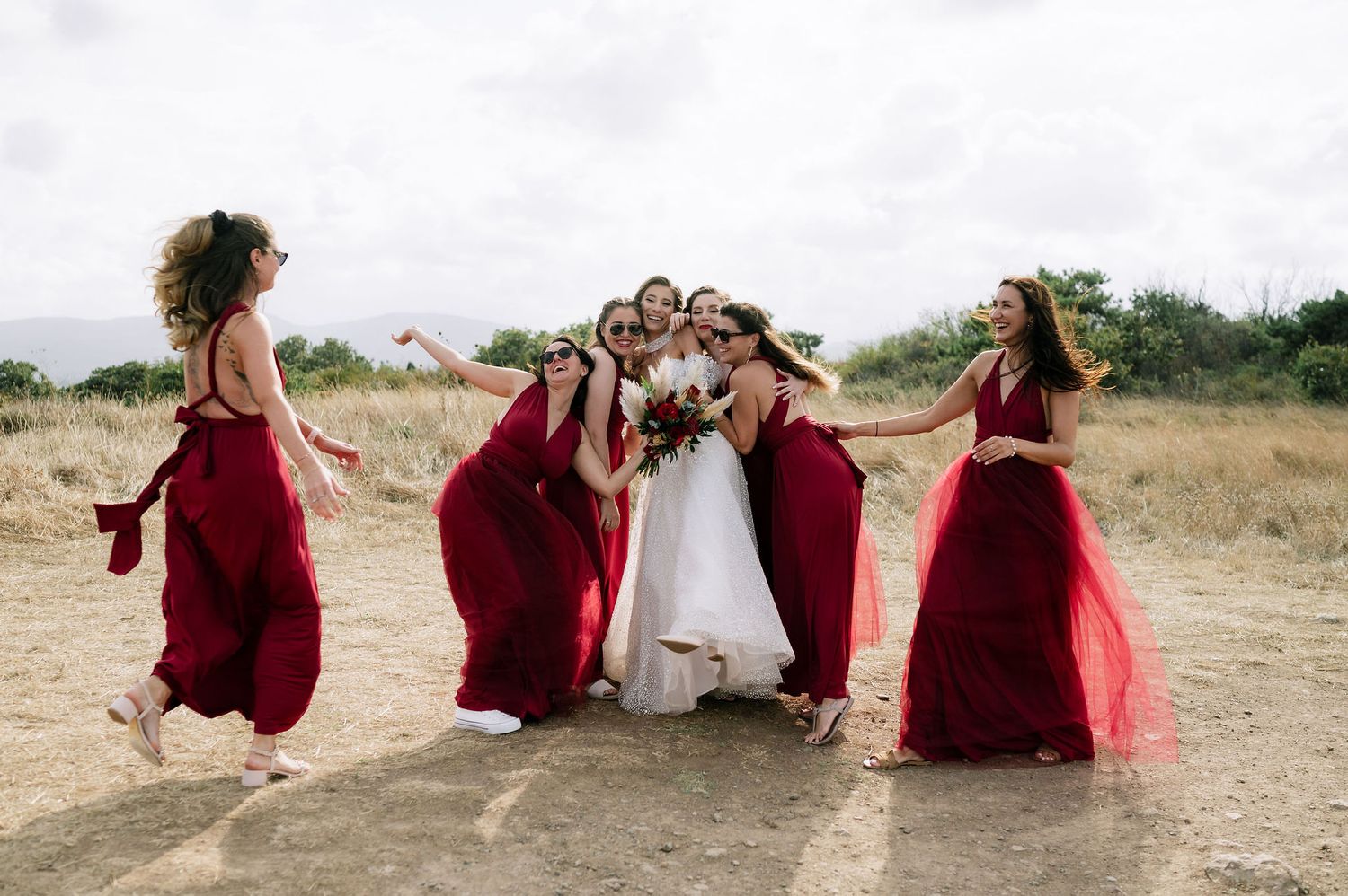 Wedding party relaxes on hillside in coordinated burgundy and white attire.