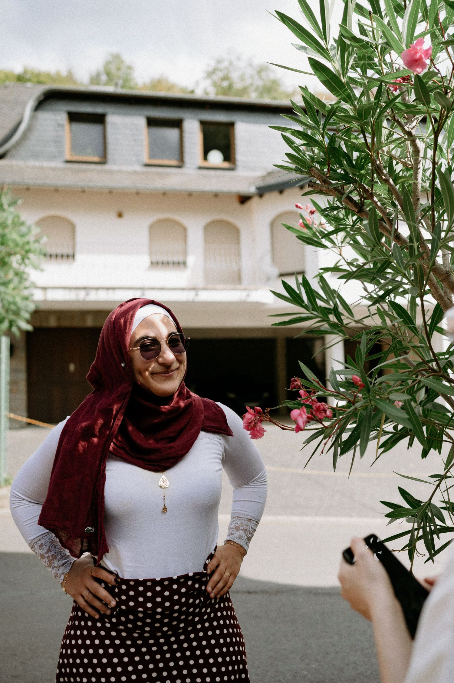 Flowering oleander bushes frame a white building exterior with burgundy accents.