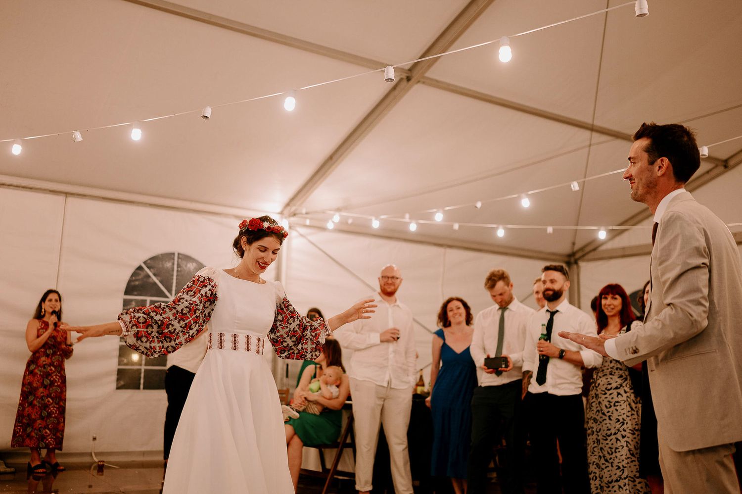 Wedding reception guests dancing together under string lights in a white tent venue.