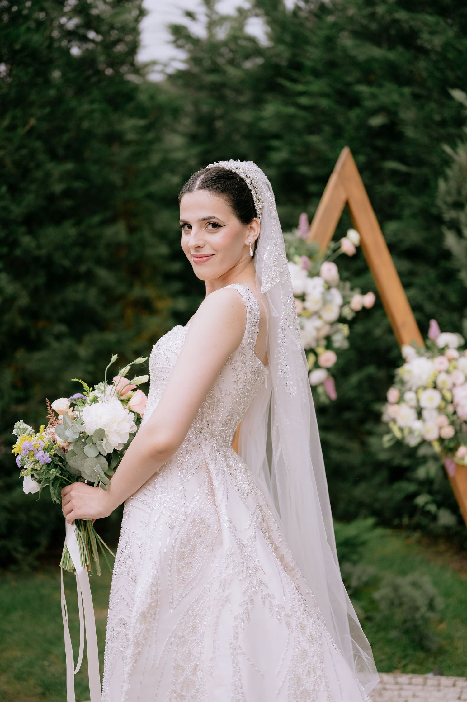 Romantic bridal portrait showcasing delicate lace details and flowing veil against greenery backdrop.