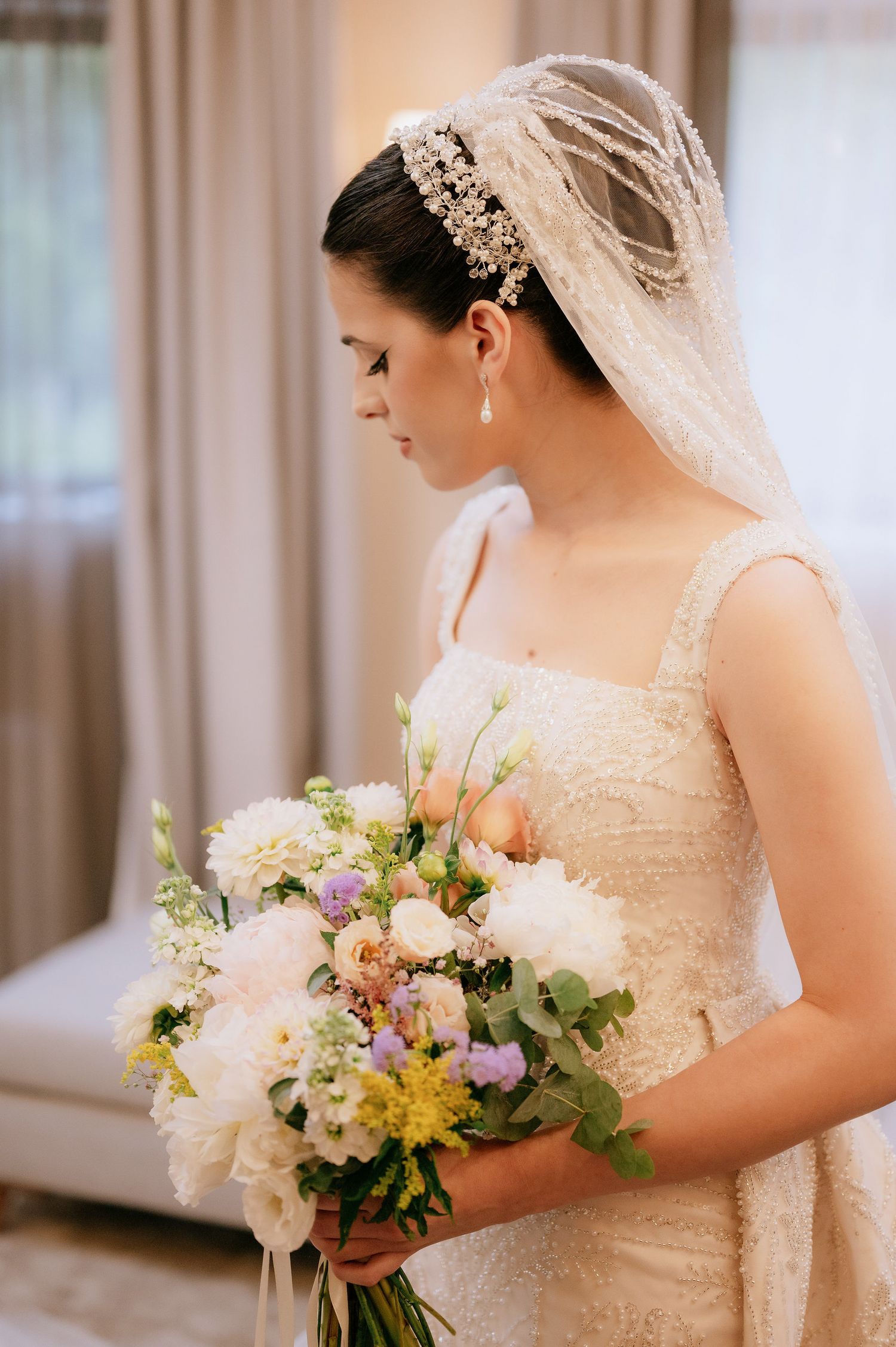 Side profile of bride with ornate headpiece holding delicate bouquet of mixed flowers.