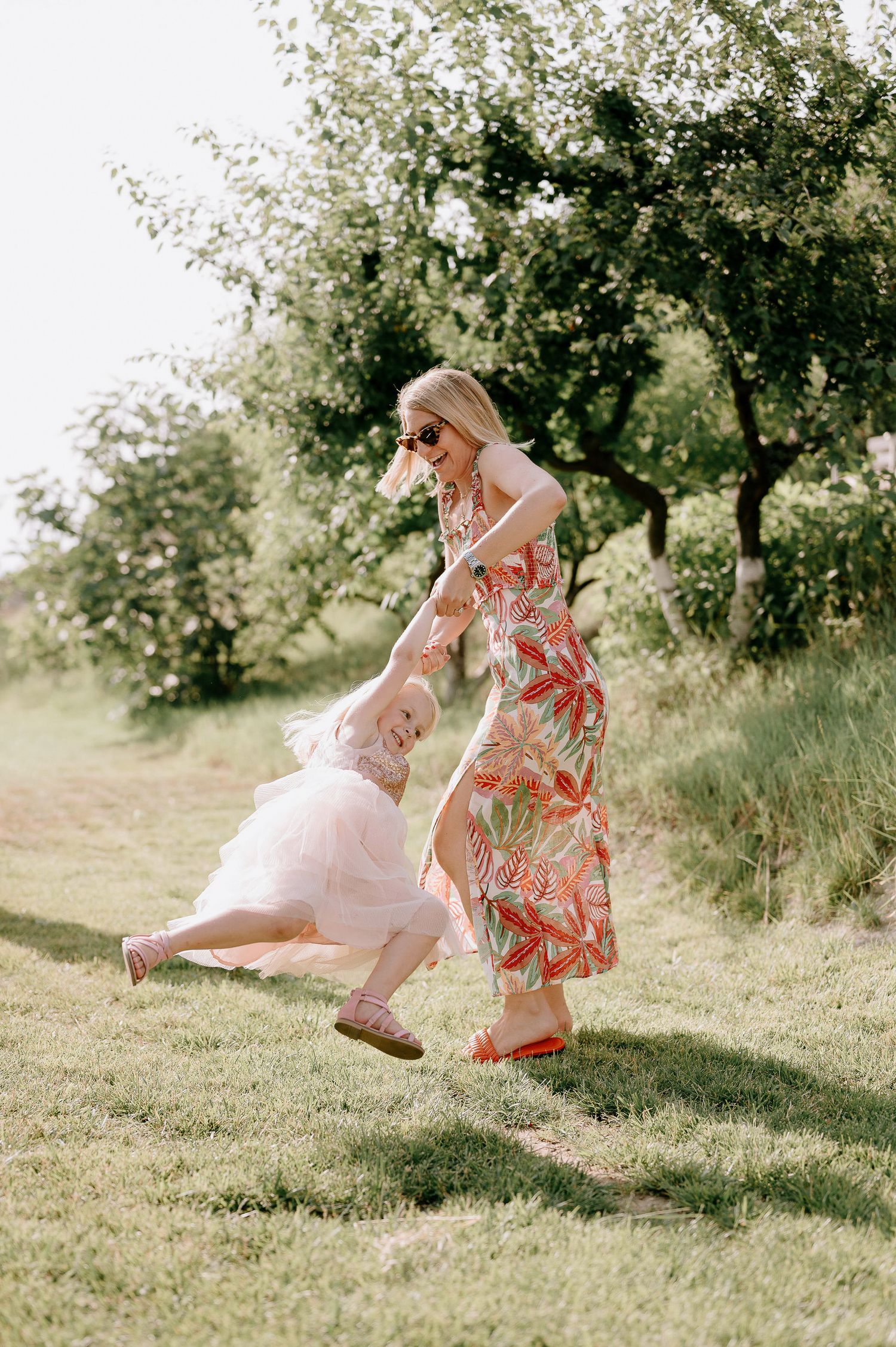 Person in a floral dress twirling playfully on a grassy hillside.