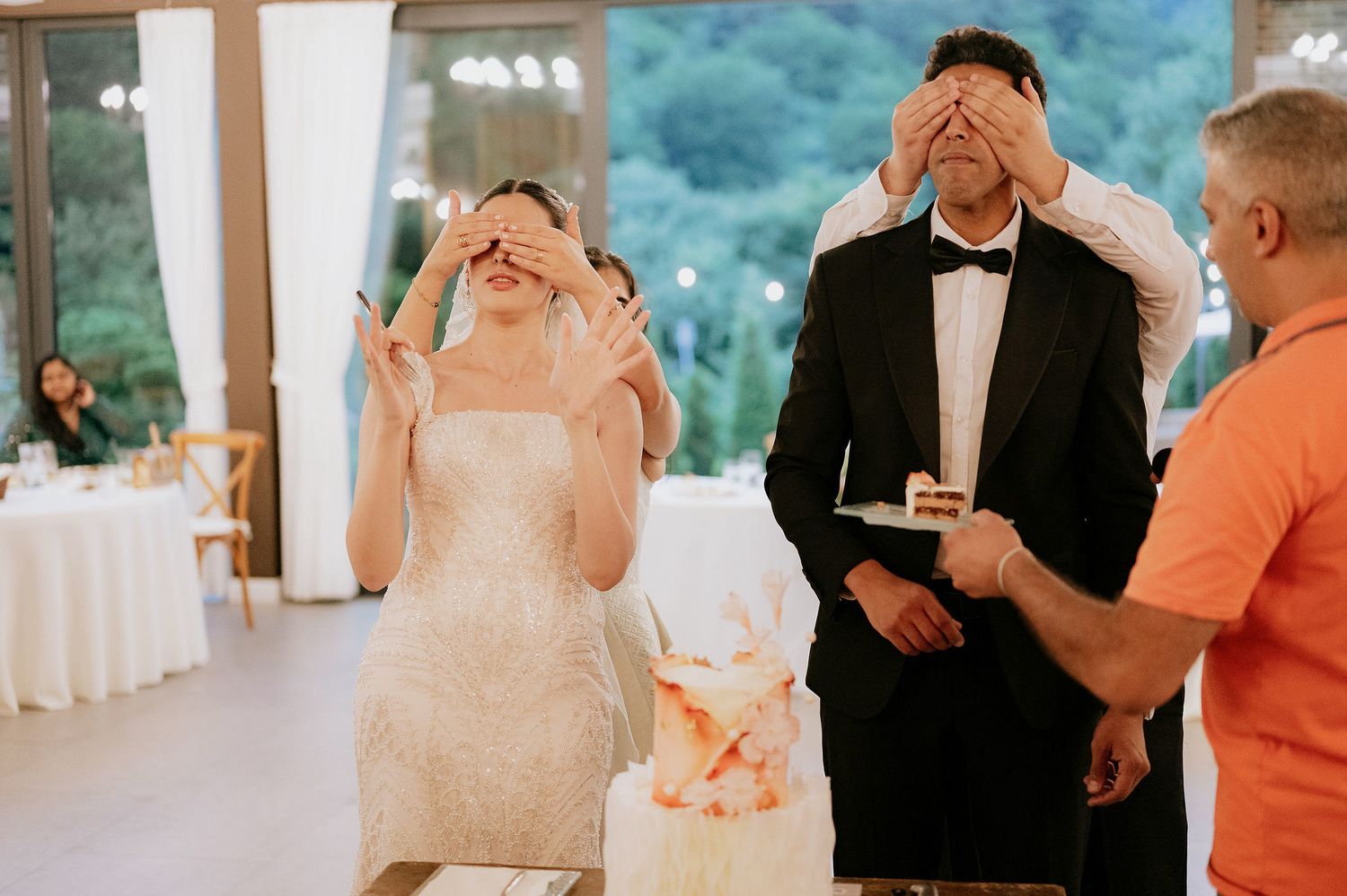 Wedding celebration moment captured in a bright reception venue with large windows.
